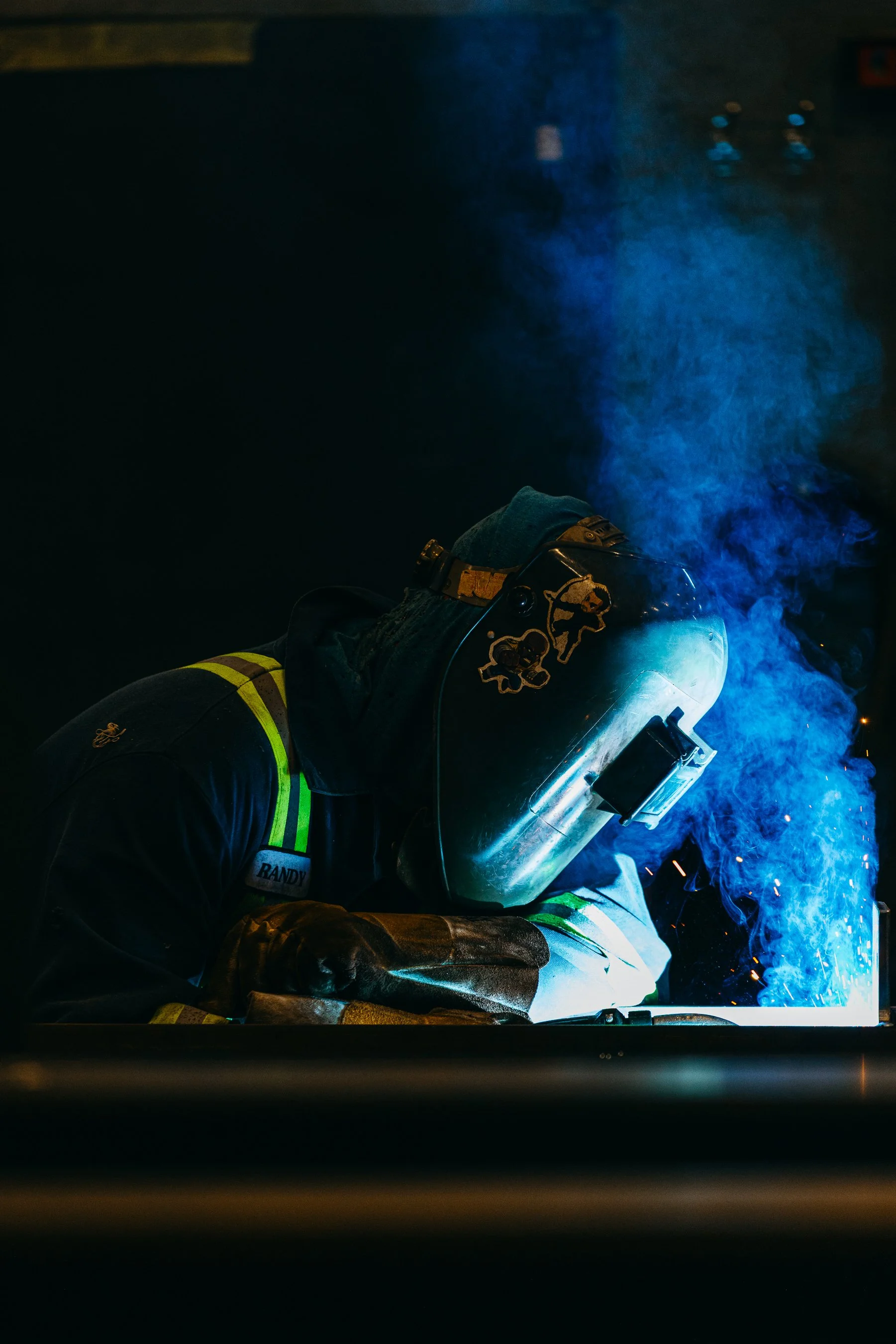 A firefighter wearing protective gear and helmet welding, with bright sparks and smoke visible.