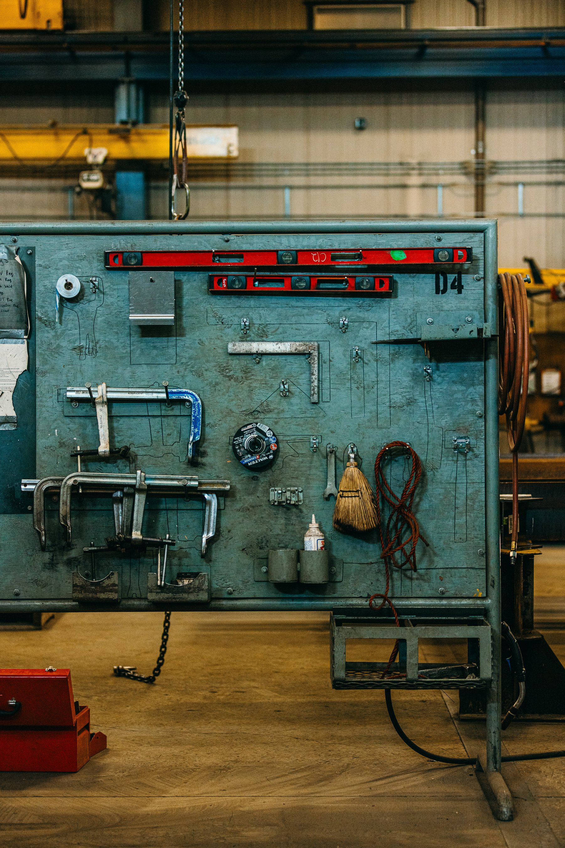 A metal workbench with various tools and supplies hanging on it or placed nearby inside a workshop or garage.