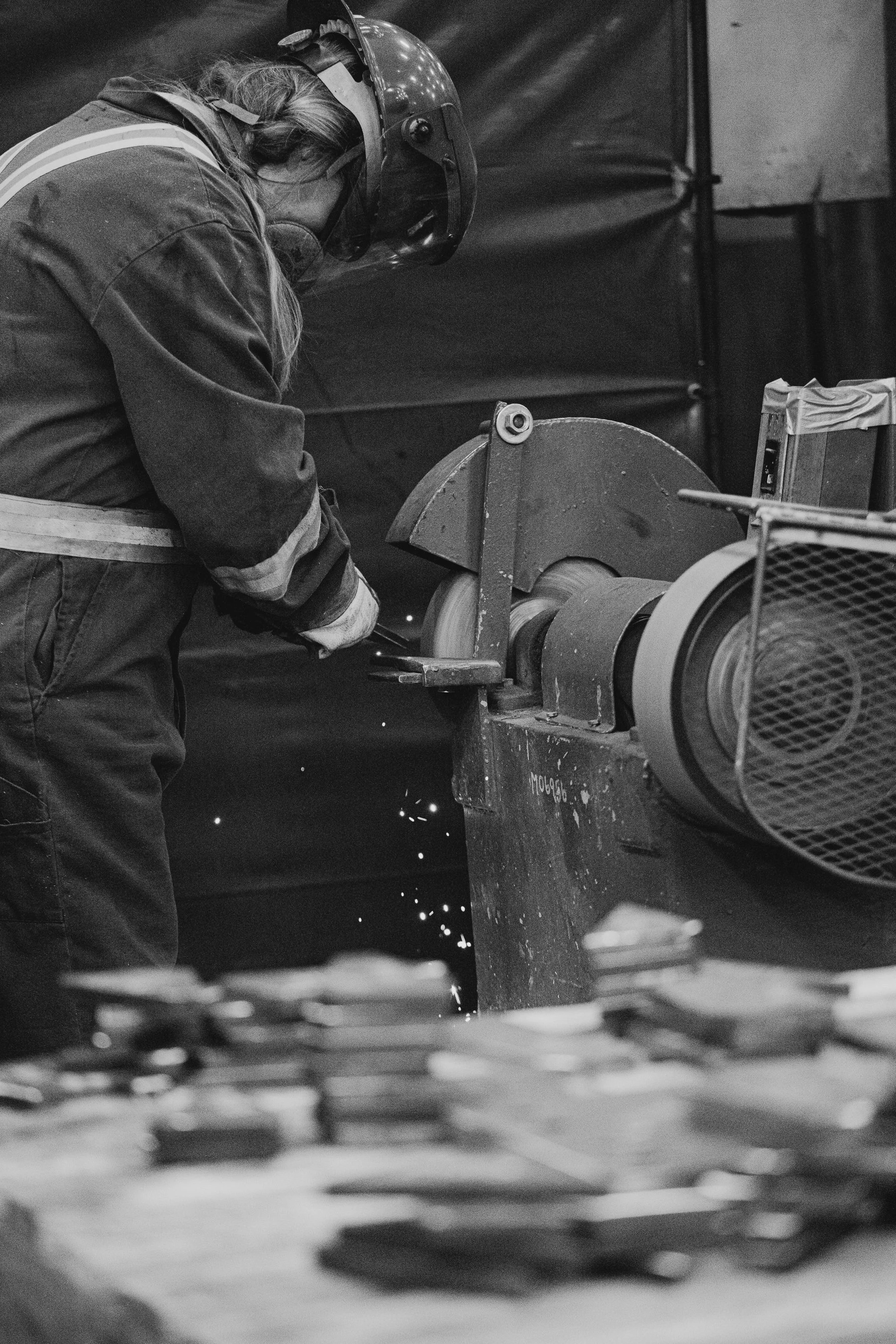 A worker wearing safety gear, including a helmet and face shield, is operating a grinding machine, producing sparks.