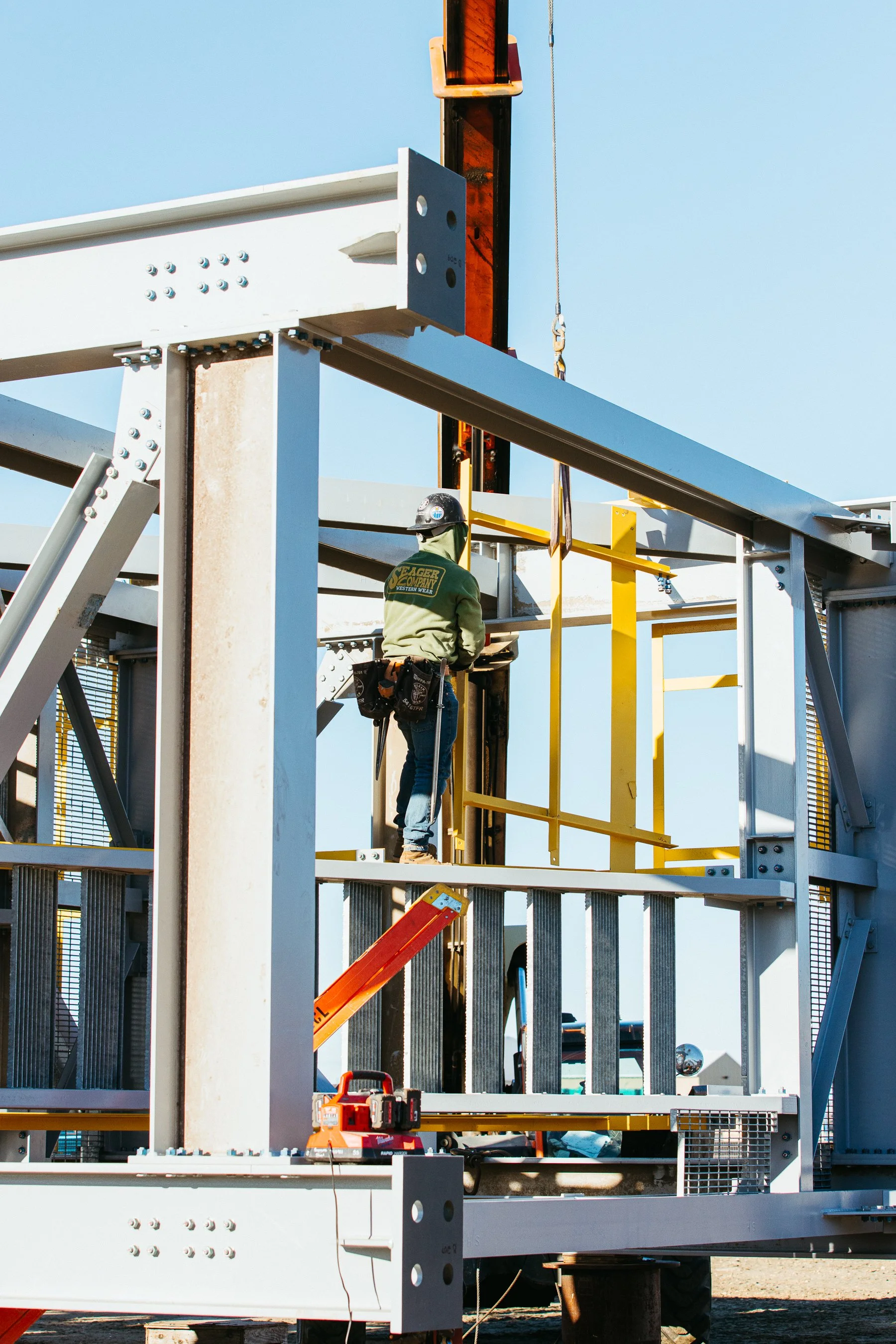 Construction worker wearing safety gear working on steel framework of a building during daytime.