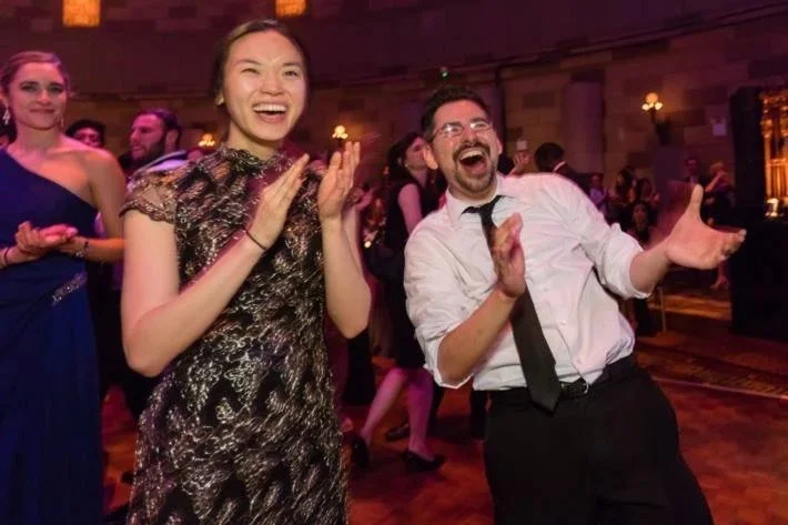 People dancing and laughing at a party or celebration in an elegant venue.