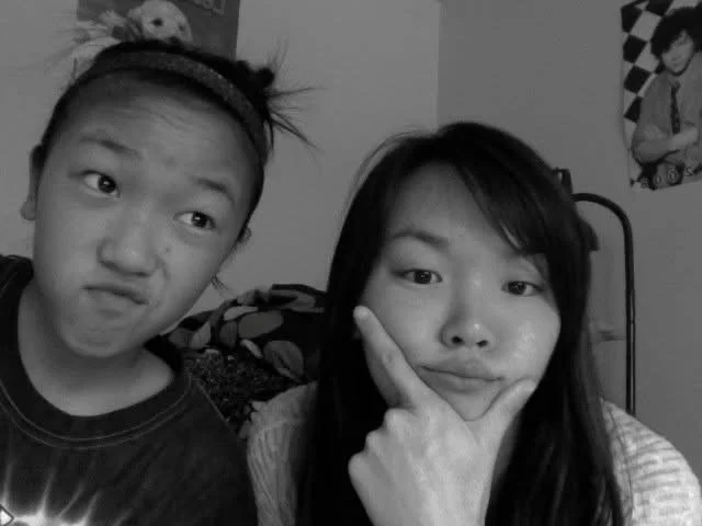 Two young women making playful expressions in a room with posters on the wall.