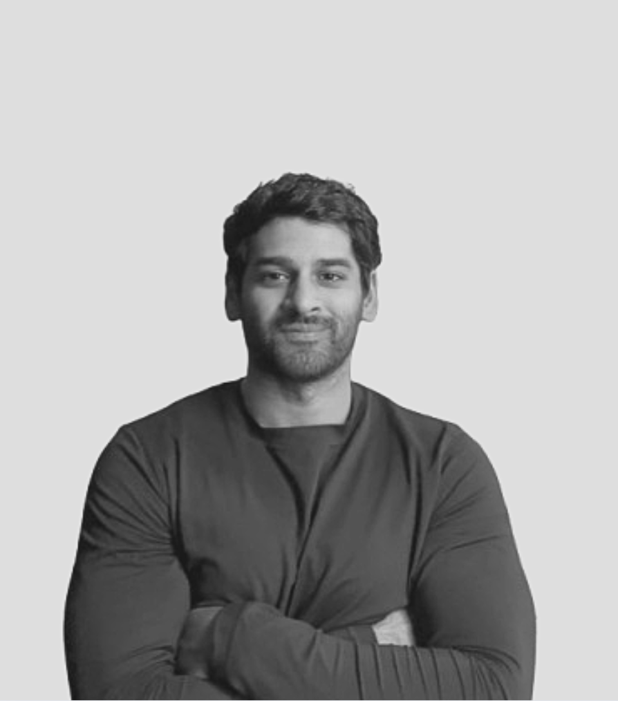 Black and white portrait of a young man with arms crossed, smiling slightly, wearing a long-sleeved shirt against a light background.