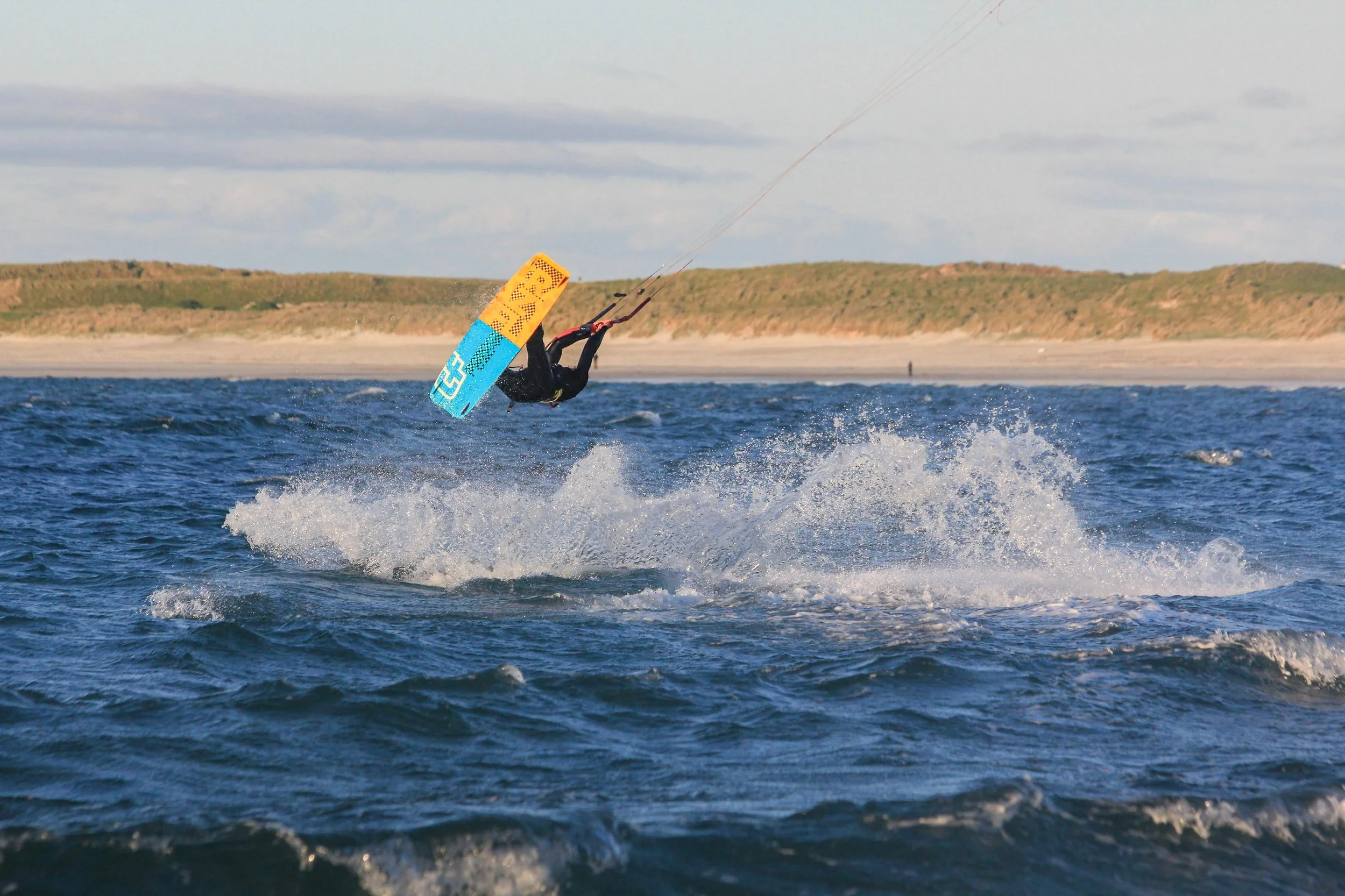 A person kiteboarding over the ocean waves with a colorful kite, performing a jump as water splashes below.
