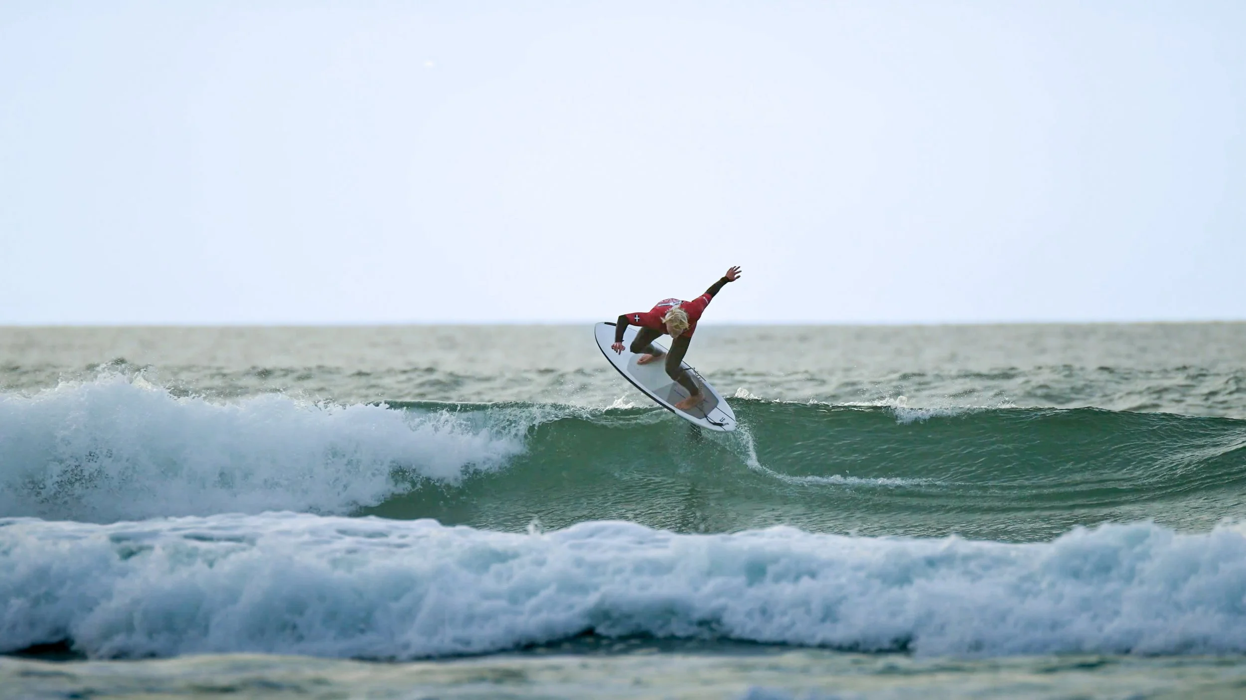 A person with blond hair surfing on a hydrofoil performing a technical turn on the wave.