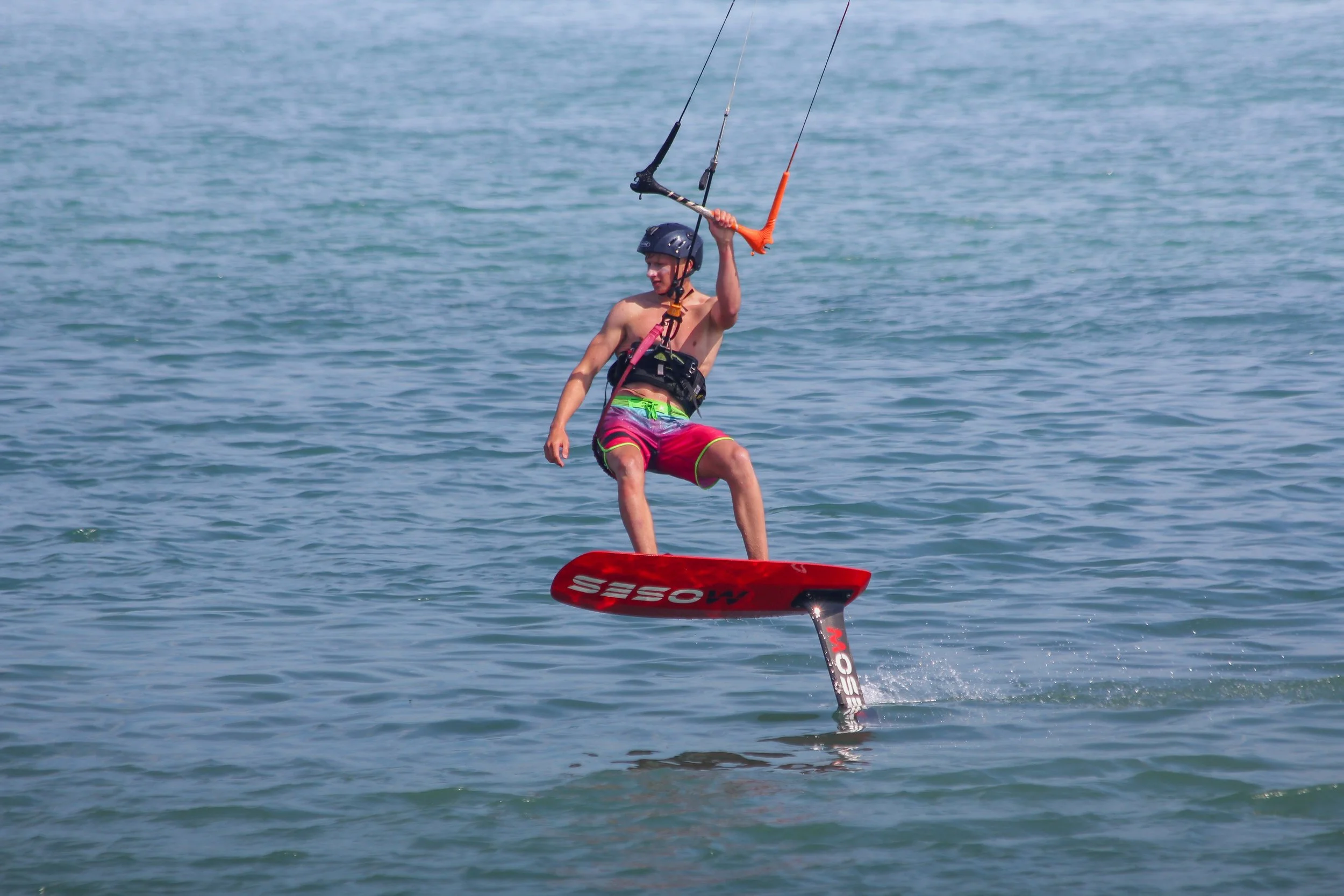 Person wearing a helmet and harness, riding a hydrofoil with a kite.