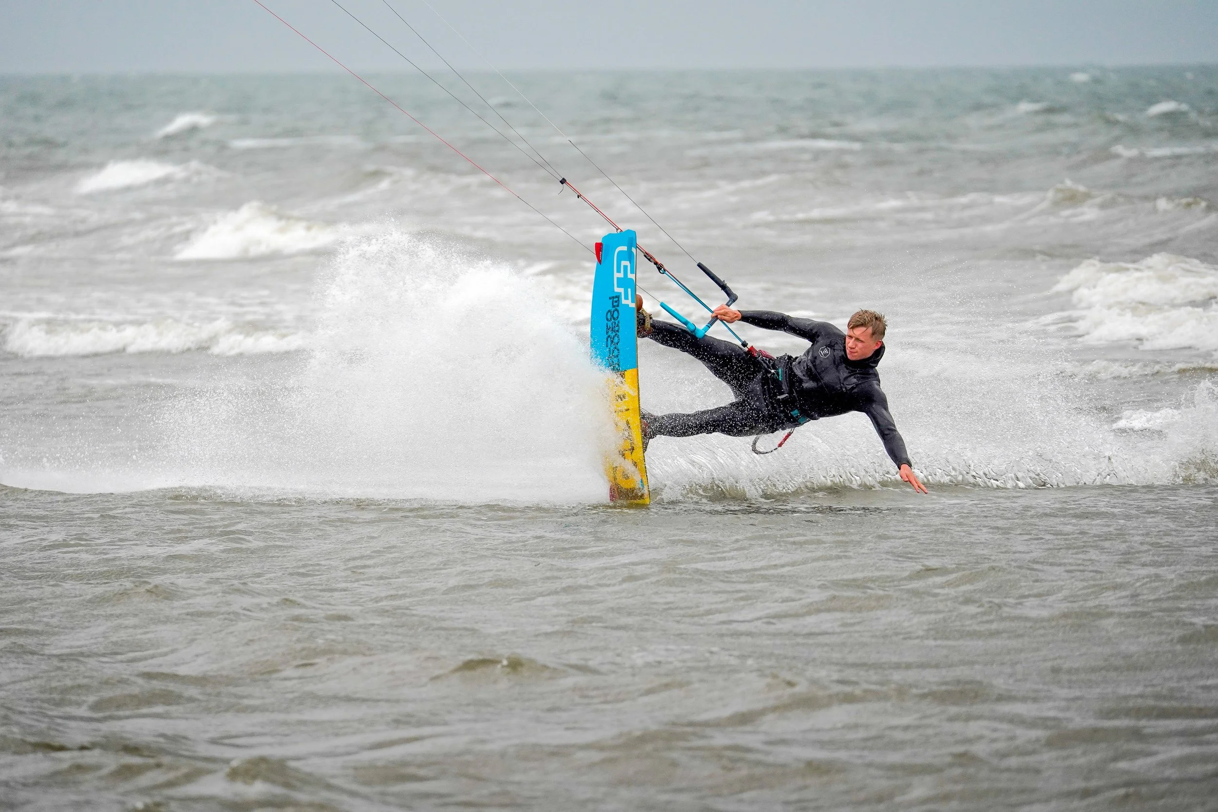 Kitesurfer sliding over the rough water with grey ocean and overcast sky.
