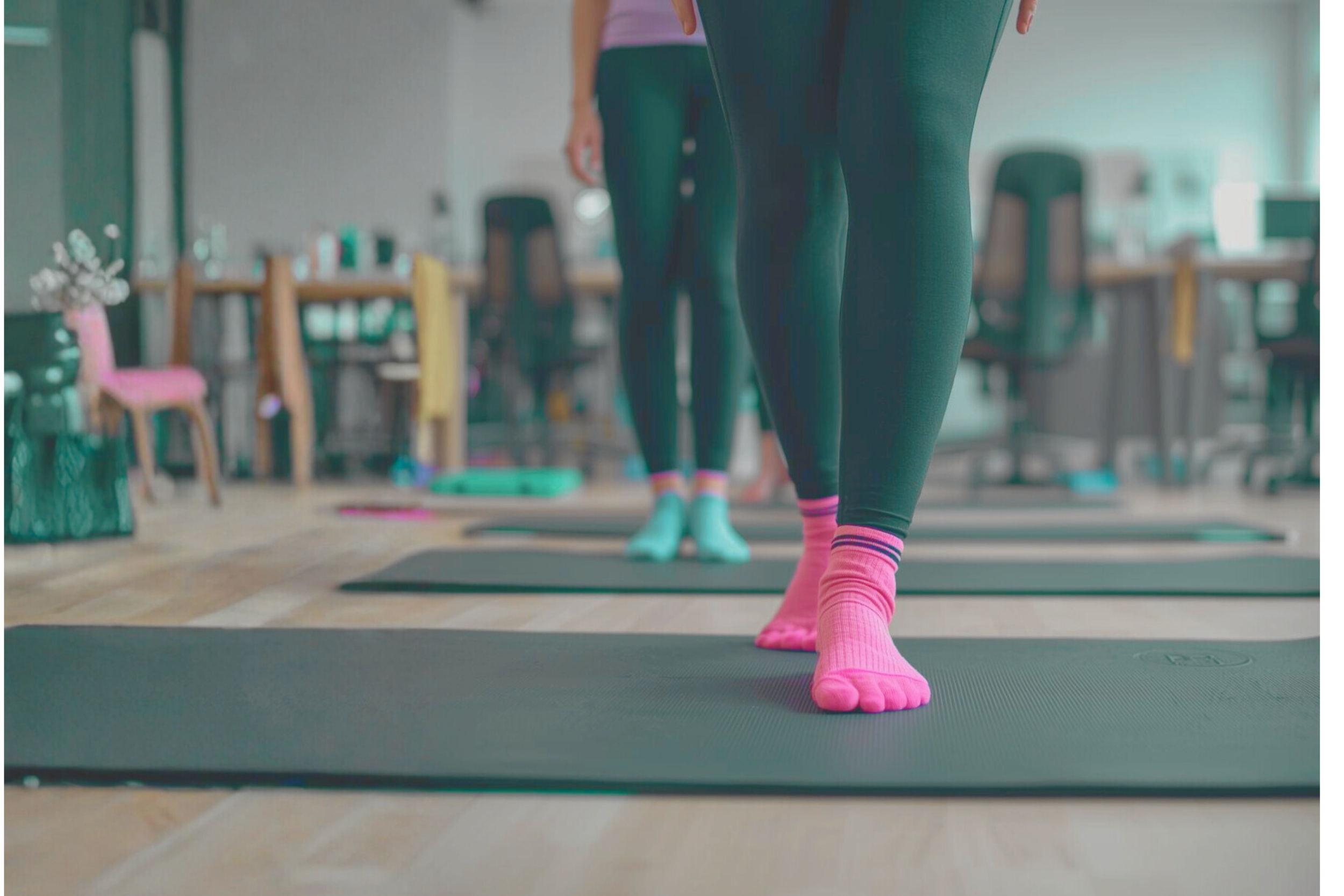 Close-up of a person wearing black leggings and pink toe socks, standing on a pilates mat in an office work setting. 