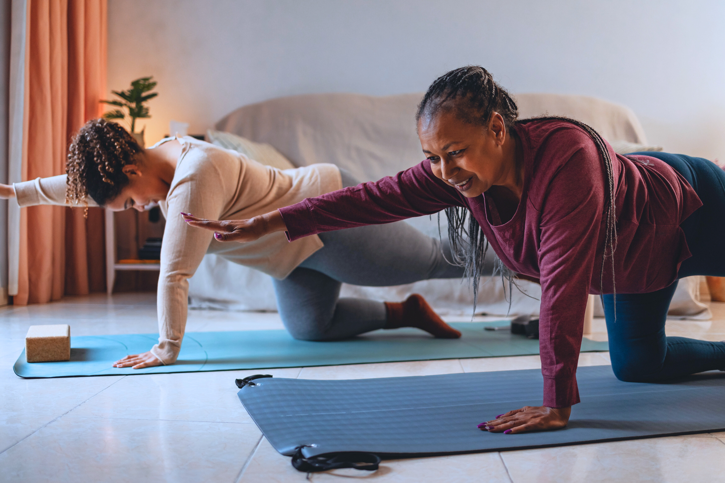 A duet pilates session where two individuals are on their hands and knees on pilates mats, performing opposite arm and leg reach exercise. The participants have  their right arm extended forward and their left leg extended backward. 