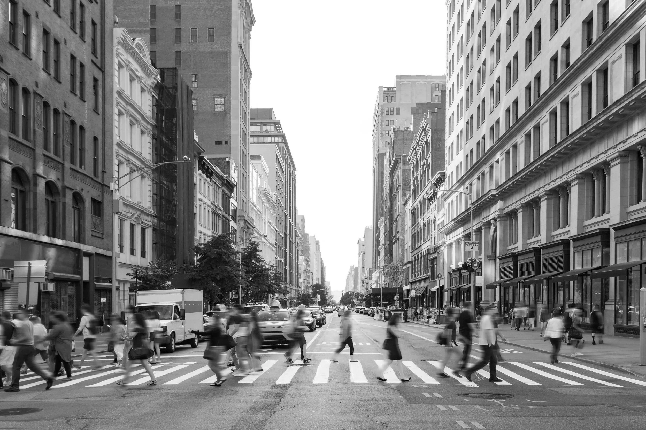 A busy street scene in New York City with pedestrians crossing at a crosswalk and  cabs driving by.
