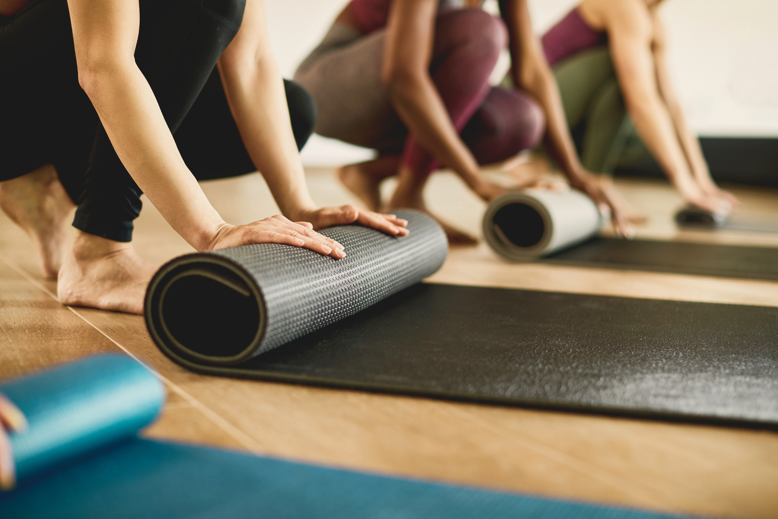 A group of people in athletic wear rolling out pilates mats on a wooden floor in a studio.