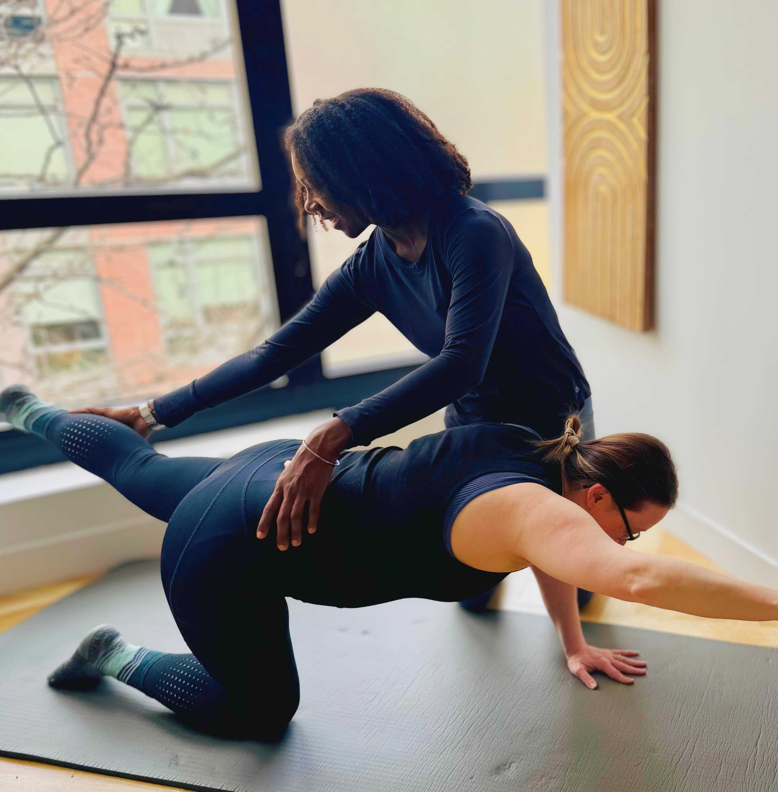 A private one on one pilates session with Courtney assisting a person in a quadruped position with one arm and the opposite leg extended on a black pilates mat. 