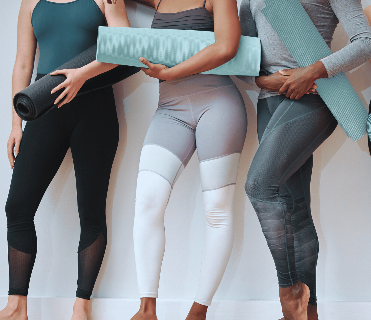 A person in athletic wear stands holding a rolled-up light blue pilates mat.