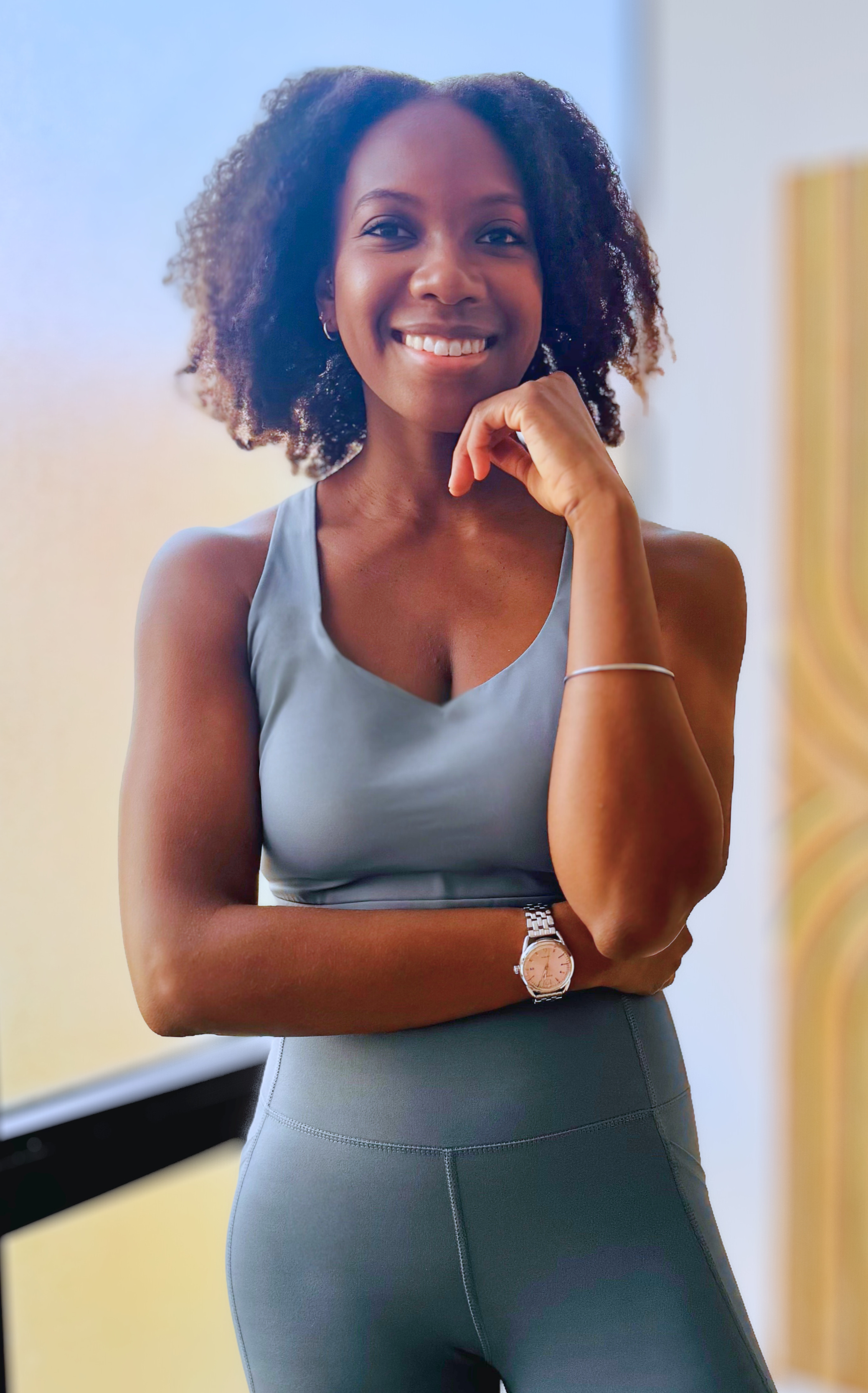Courtney, the founder of True Align Pilates, wearing grey athletic wear standing and looking into the camera while smiling and resting her chin on her hand.