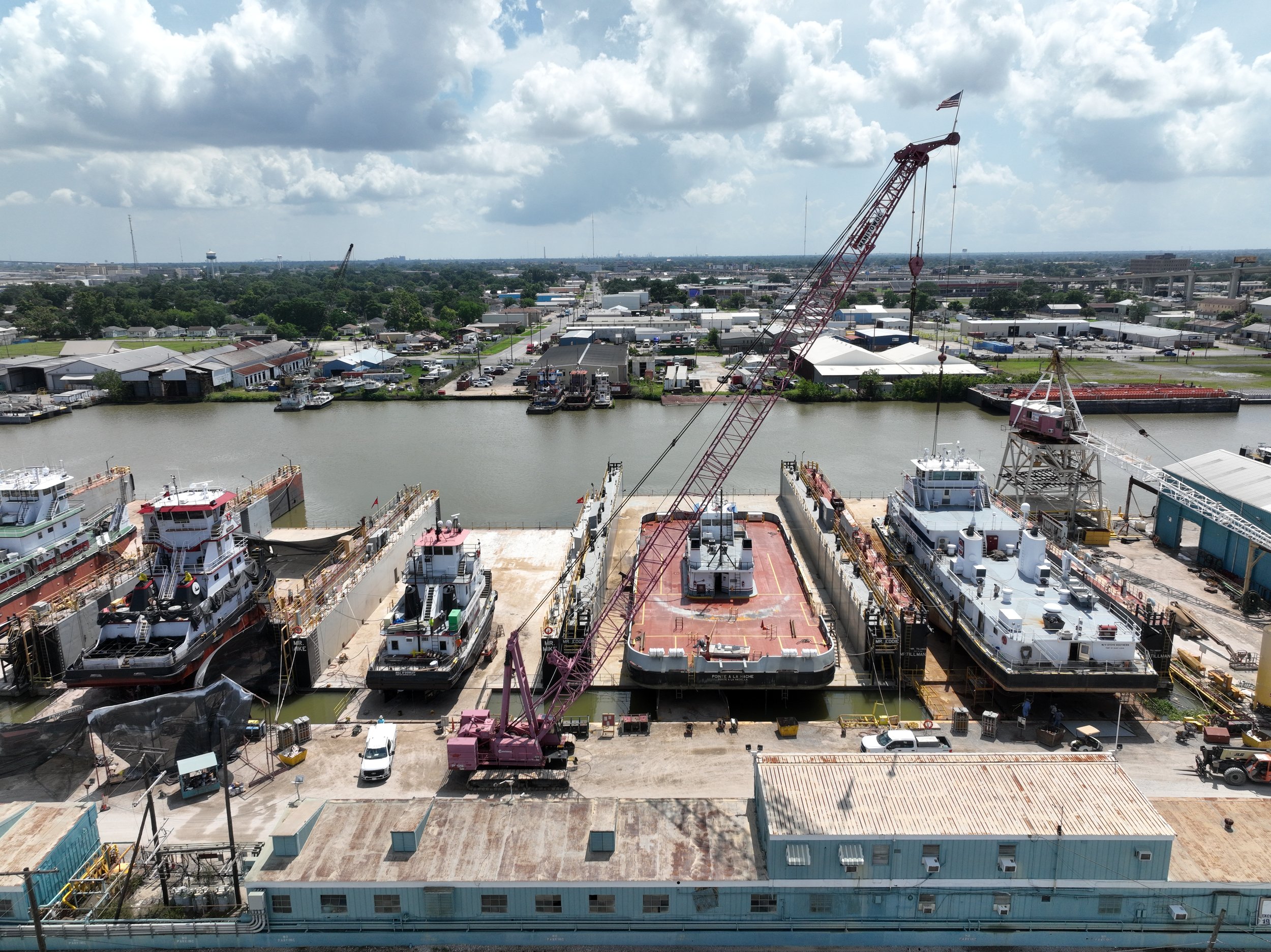 A harbor with several large ships docked, cranes in operation, and a cityscape in the background under partly cloudy skies.