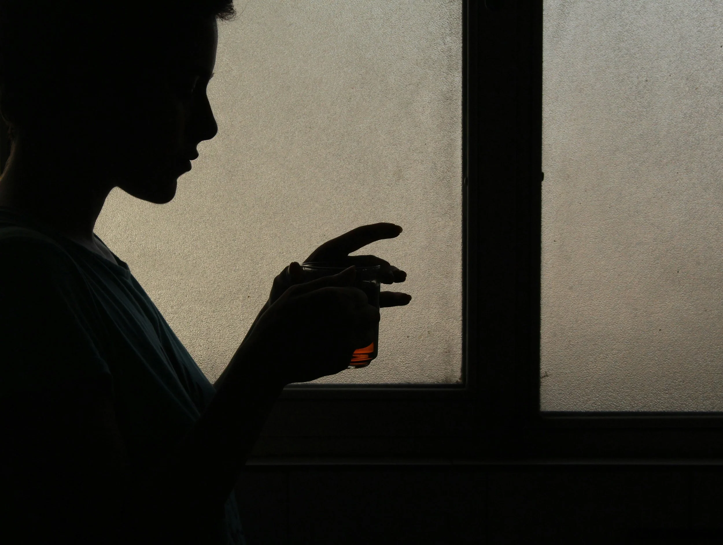 Silhouette of a woman holding a small bottle in front of a frosted window.
