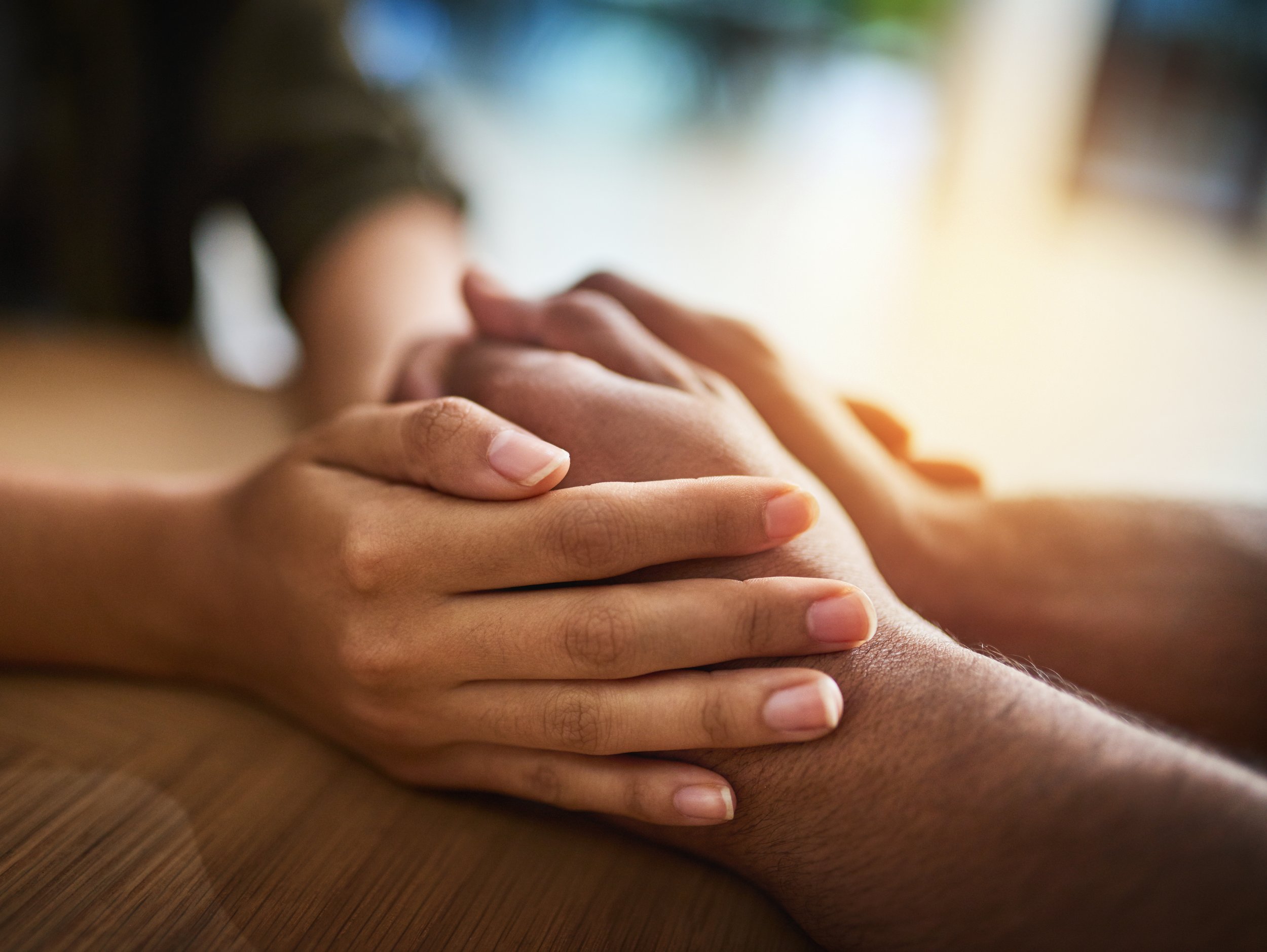 Close-up of a couple holding each others hands over a table as they sit across from one another.