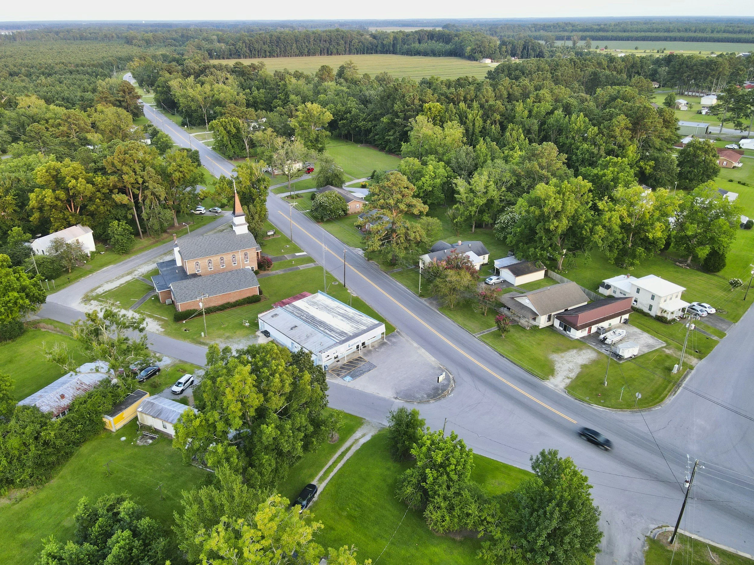 Aerial view of a small town with a church, various houses, trees, and a main road with a car driving.