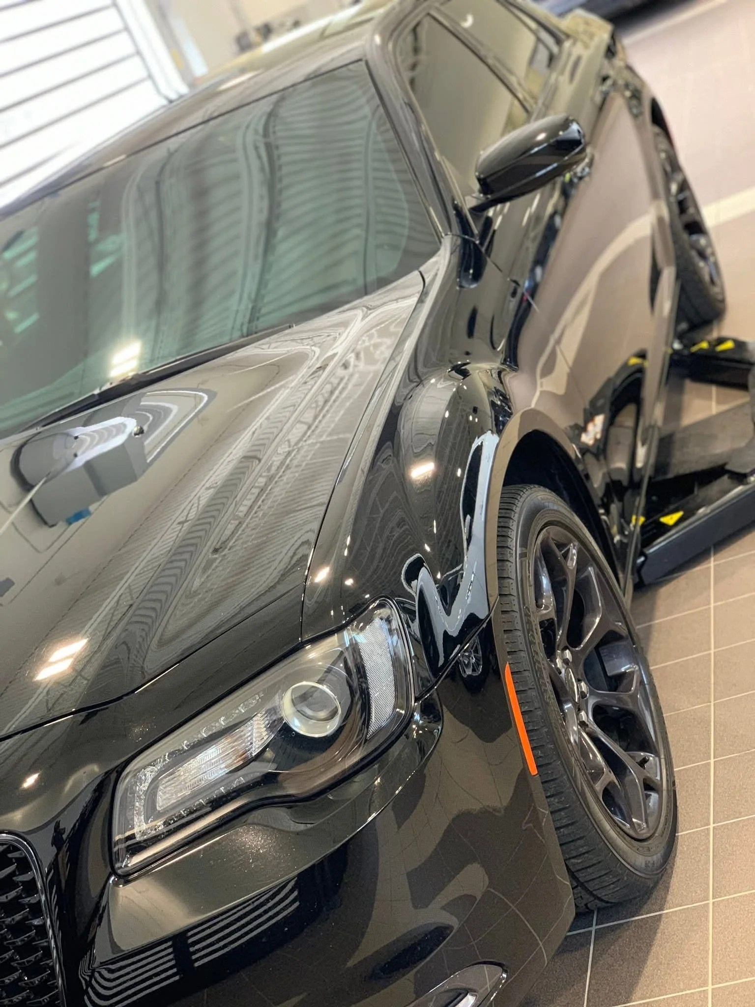 A black car with a sleek design parked indoors on a tiled floor, with yellow supports beneath the passenger side door area.