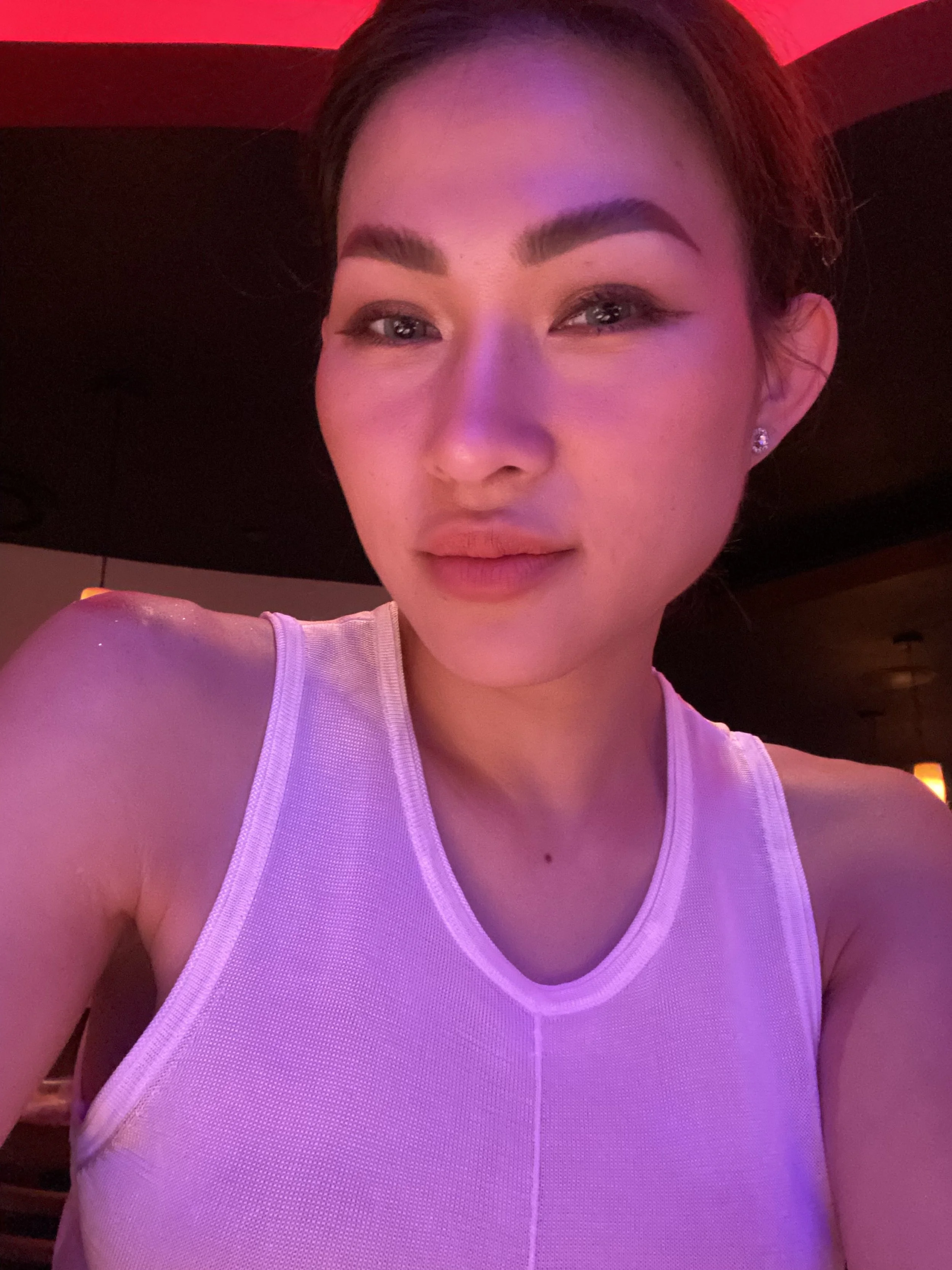 Trang T. Nguyen selfie under pink lighting, wearing a white sleeveless top and subtle glam makeup.