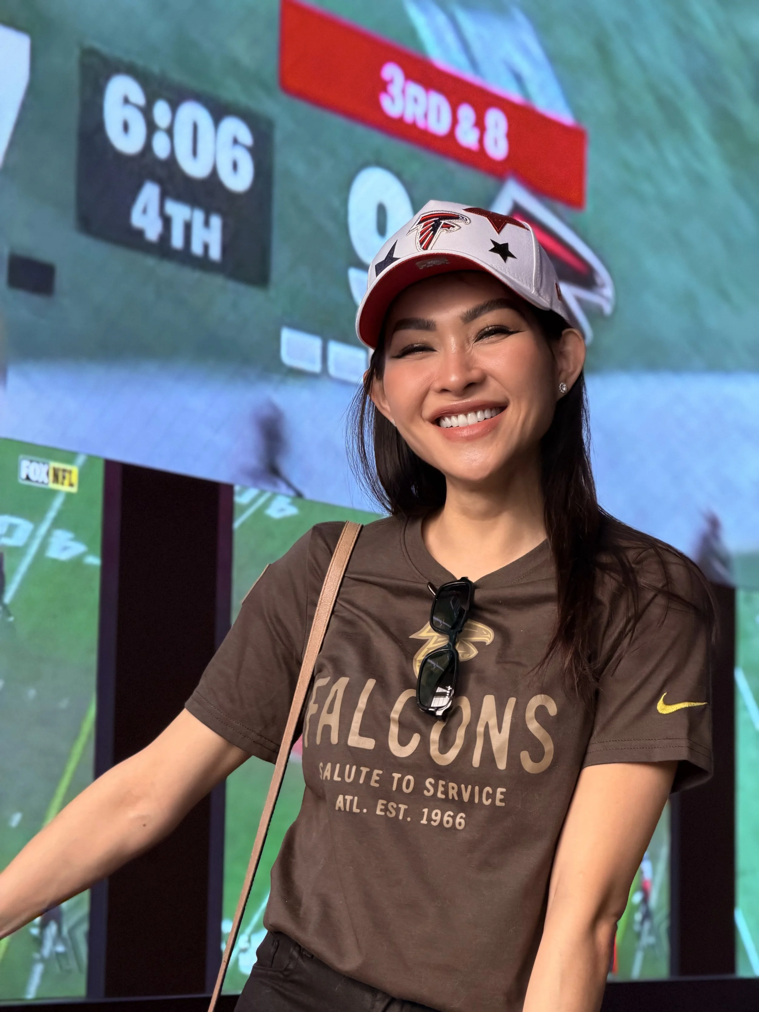 Trang T. Nguyen smiling in a Falcons cap and Salute to Service shirt in front of a football screen.