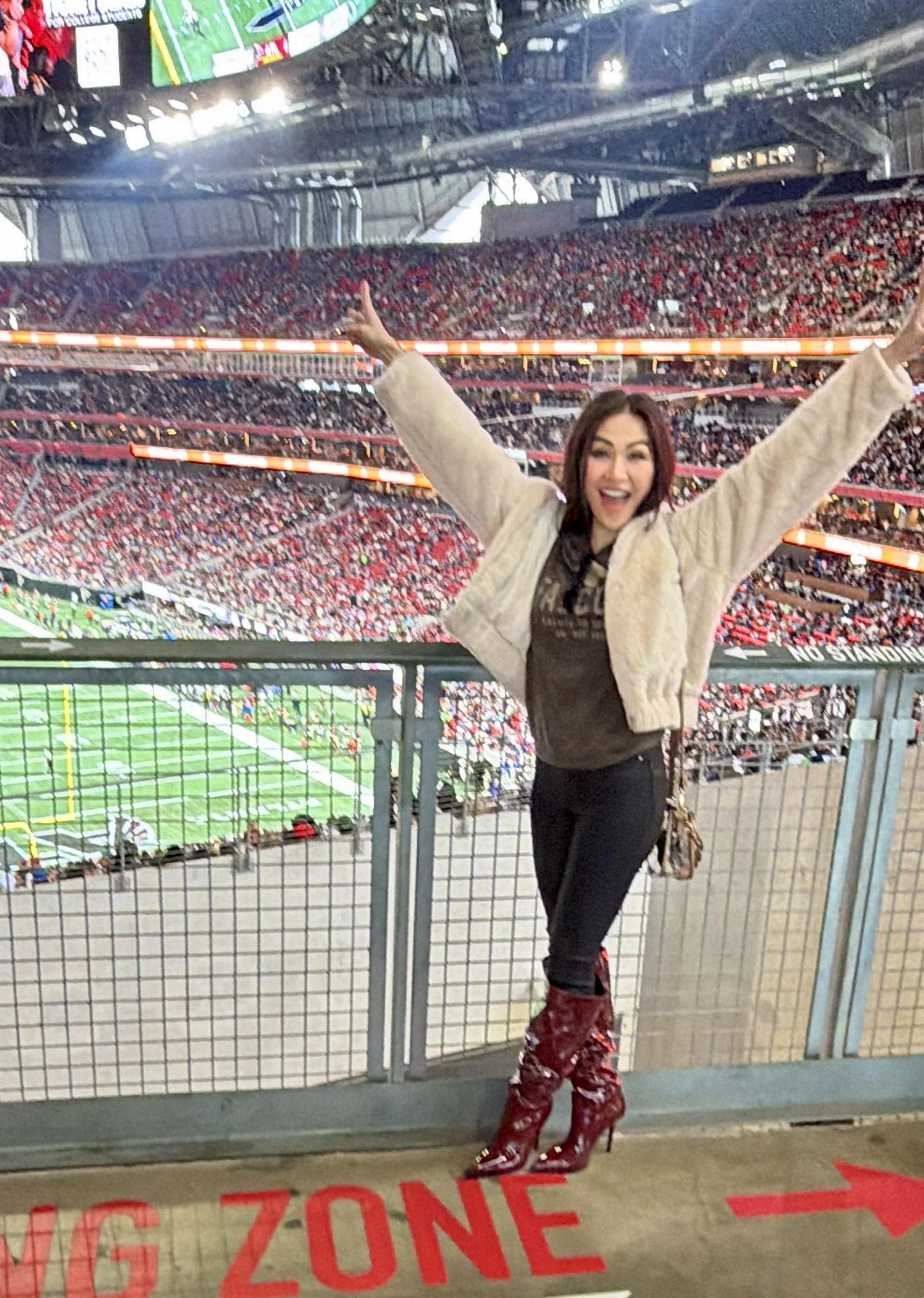 Trang T. Nguyen celebrating with arms raised at a packed football stadium near the railing.
