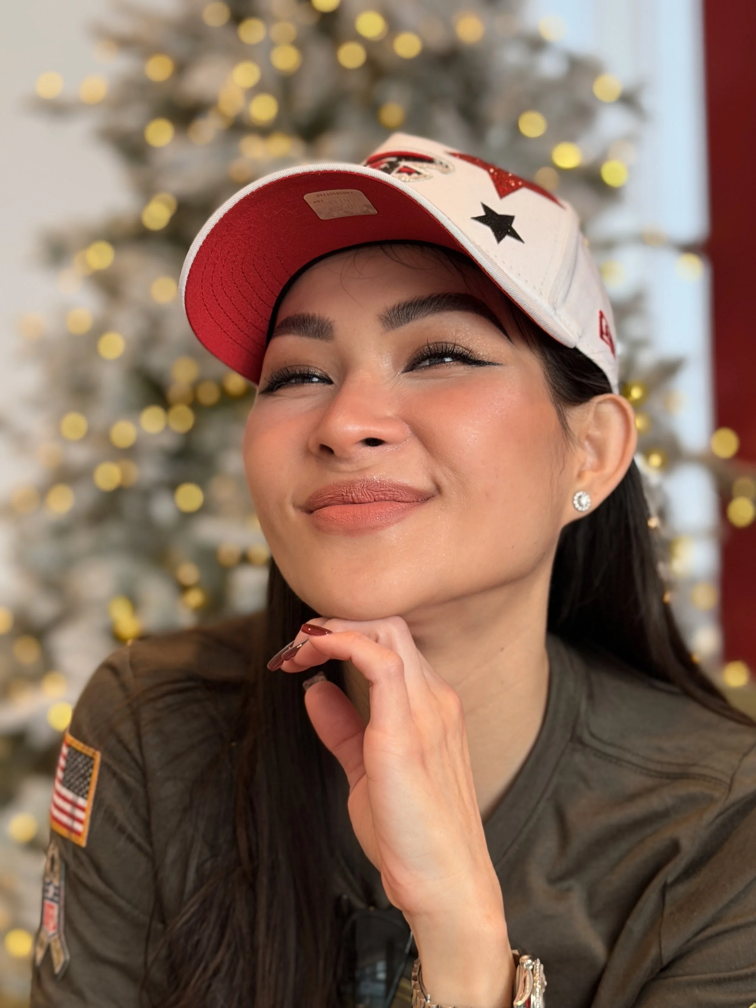 Trang T. Nguyen smiling in a Falcons cap with hand under chin, holiday lights blurred in the background.