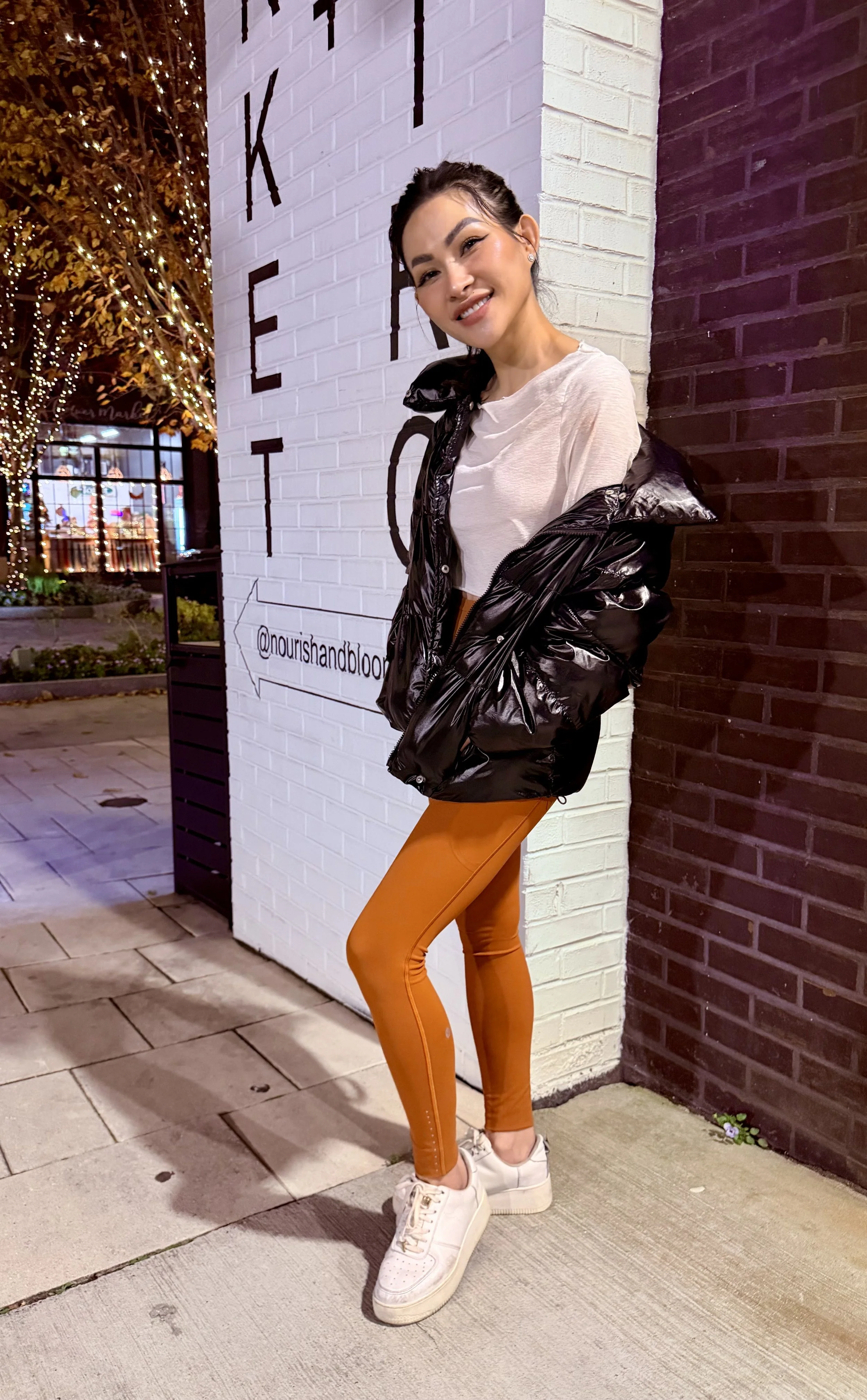 Trang T. Nguyen posing outdoors at night by a ‘Market’ sign, wearing orange leggings and a black puffer jacket.