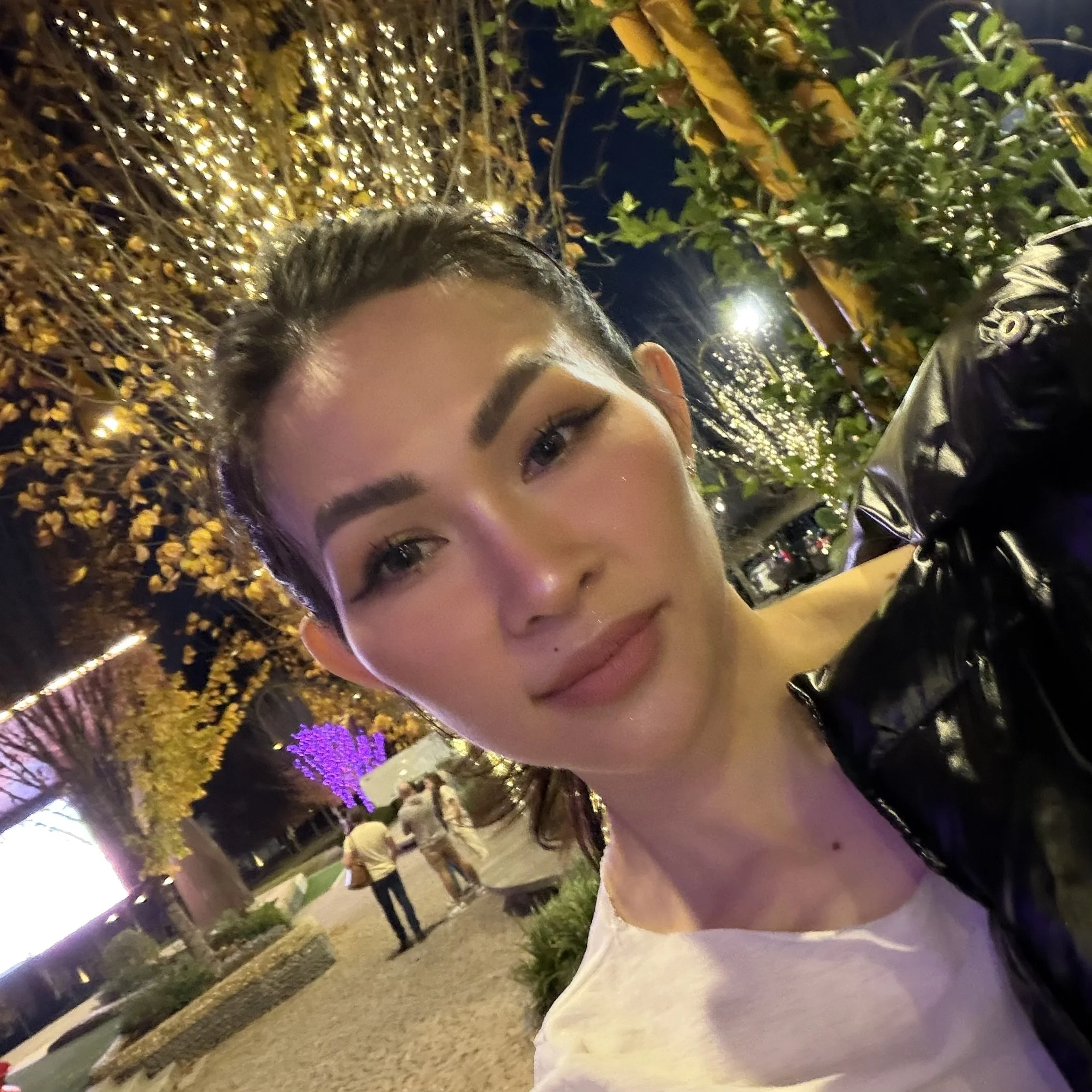 Trang T. Nguyen outdoor nighttime selfie with festive string lights and trees in the background.
