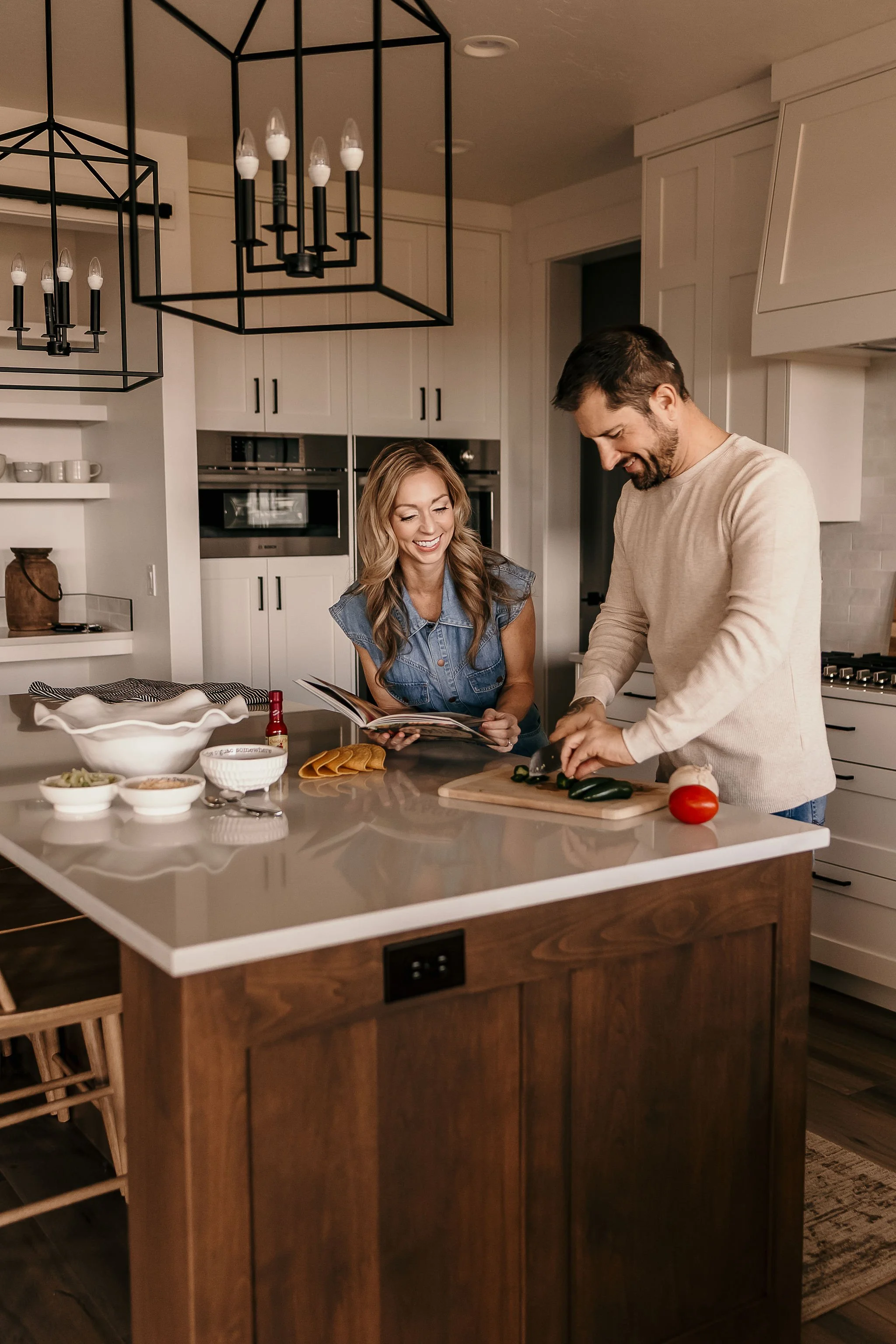 A man and woman making salsa together in a modern kitchen, chopping vegetables on a wooden cutting board, with bowls and condiments on the counter.