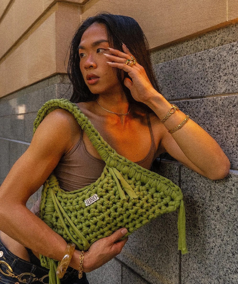 A model holds the Cider Staple JUNO Crochet bag, leaning against a wall.