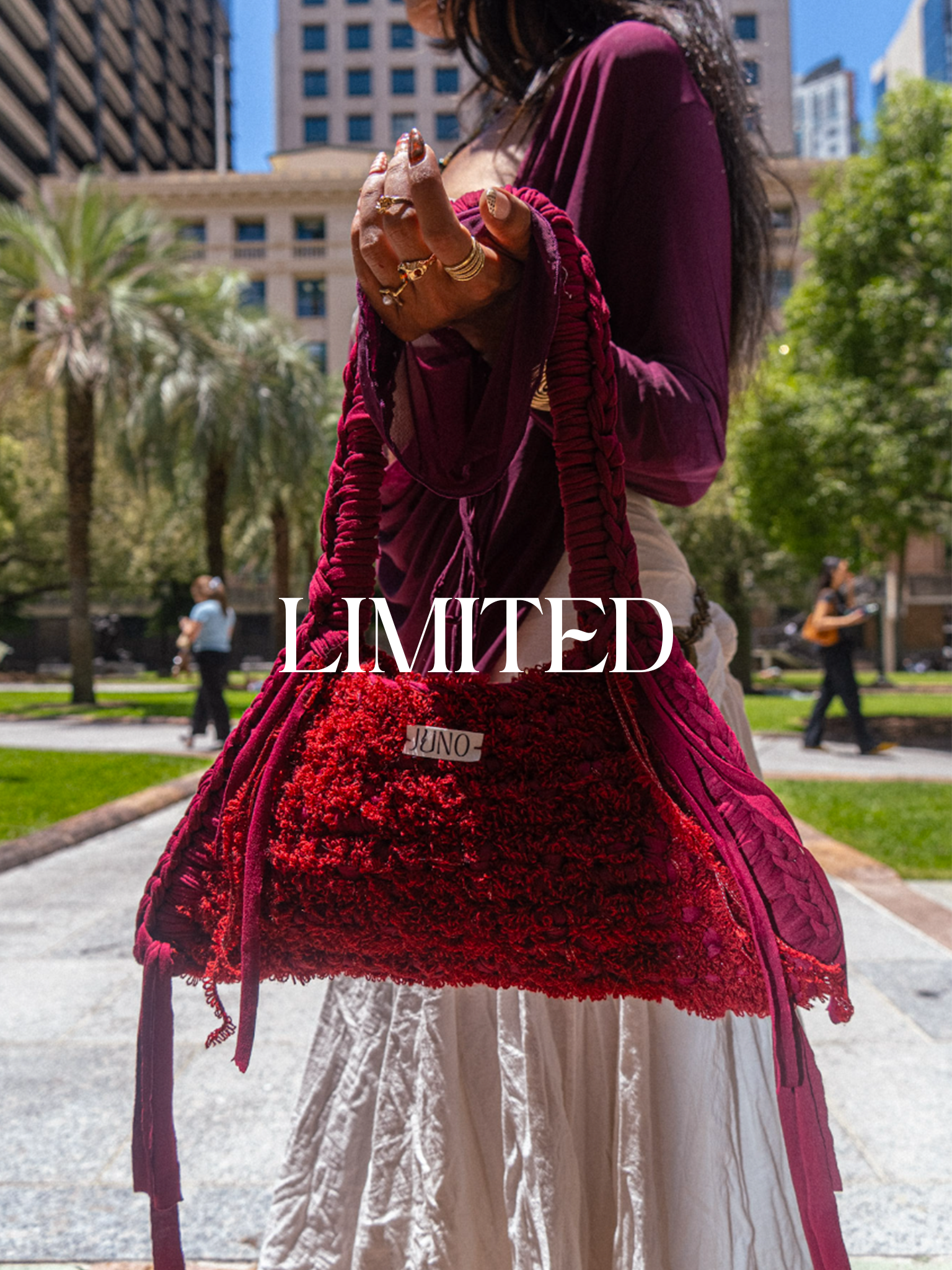 A model holding the limited Anemone bag in an outdoor park with an urban cityscape in the background. 
