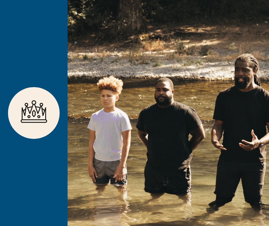 Three males standing in a shallow river with trees in the background during daytime.