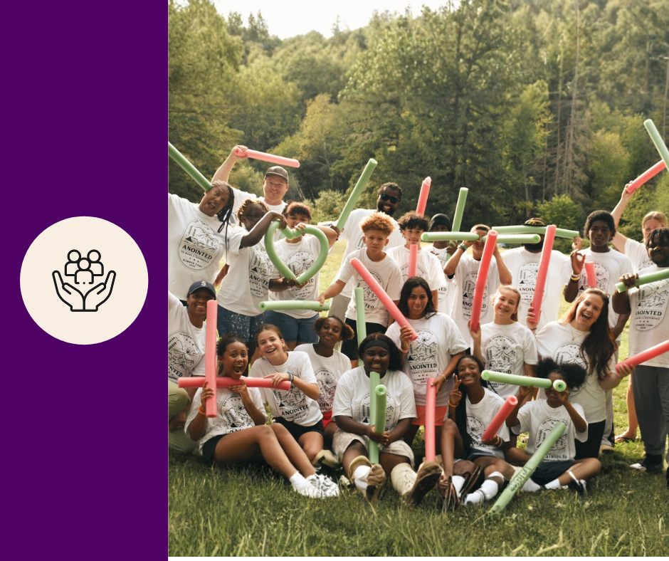 A large group of children and teenagers outdoors holding colorful foam sticks, posing happily with a Nature VBS logo in the background.