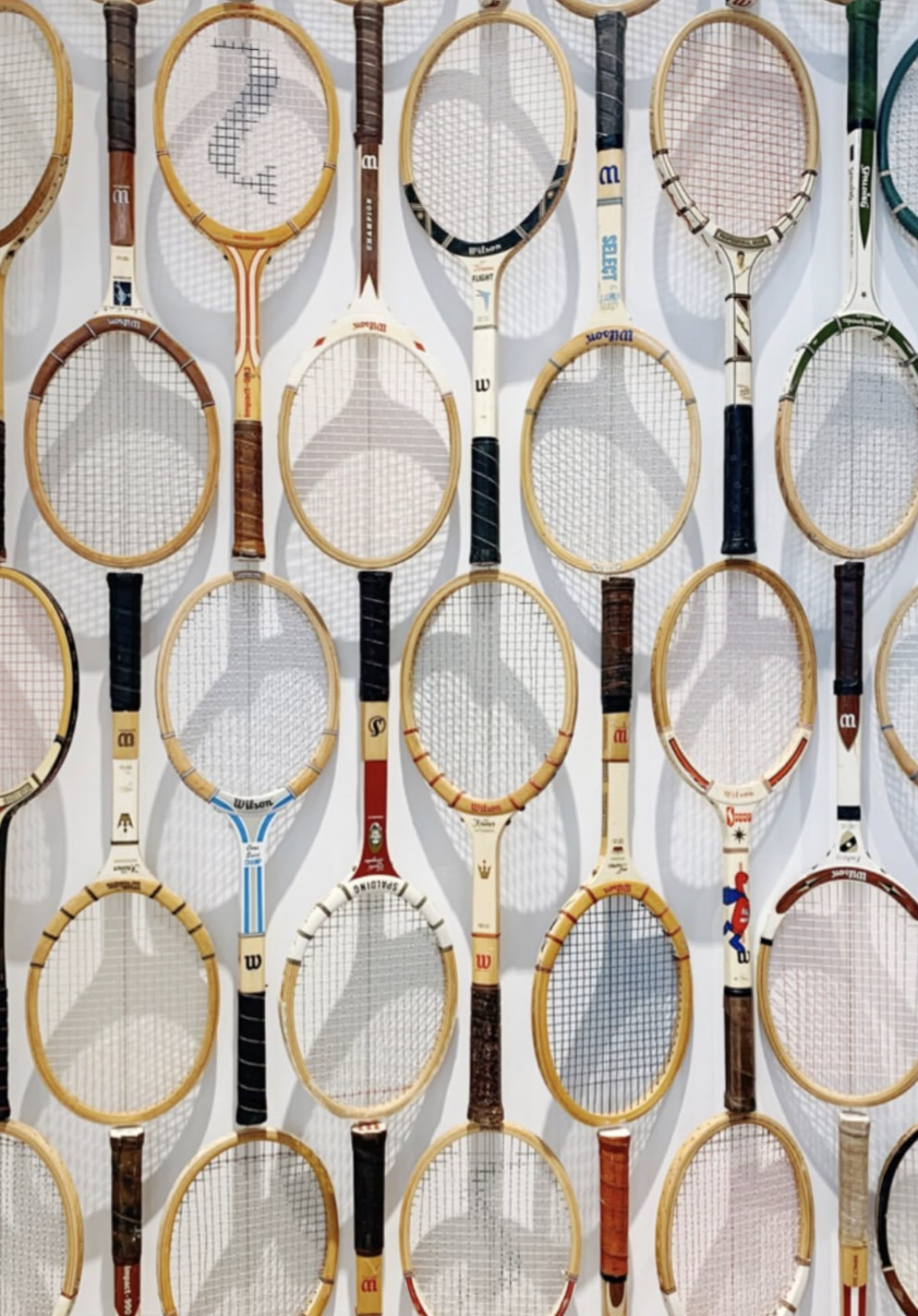 Multiple vintage wooden tennis rackets mounted on a white wall.