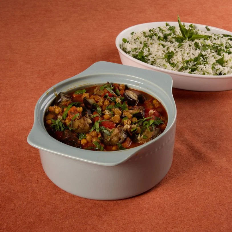 A bowl of vegetable curry and a bowl of cilantro lime rice on a wooden table.