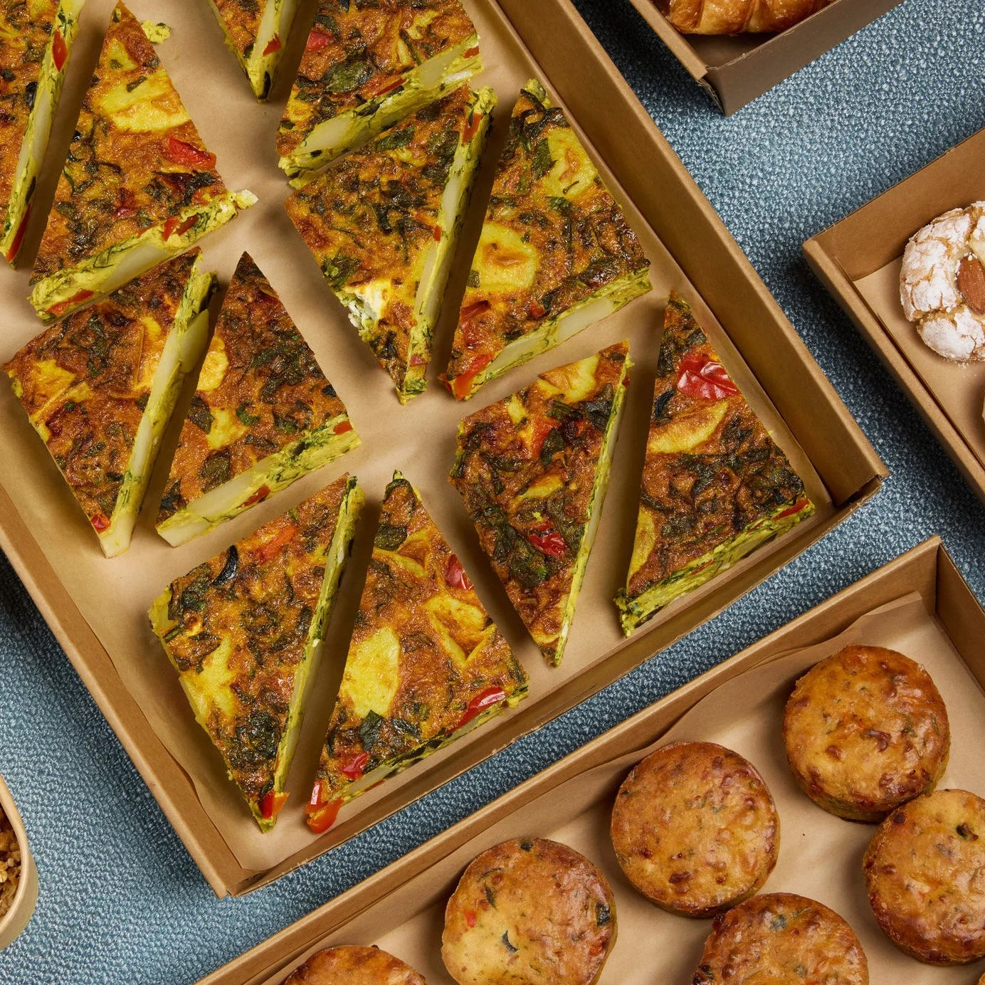 Slices of vegetable frittata with red peppers and spinach in a cardboard tray.