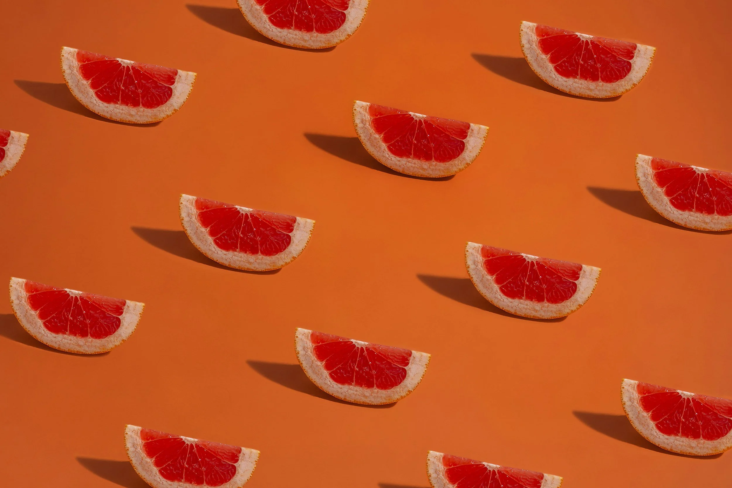 Slices of grapefruit arranged on an orange background with shadows.
