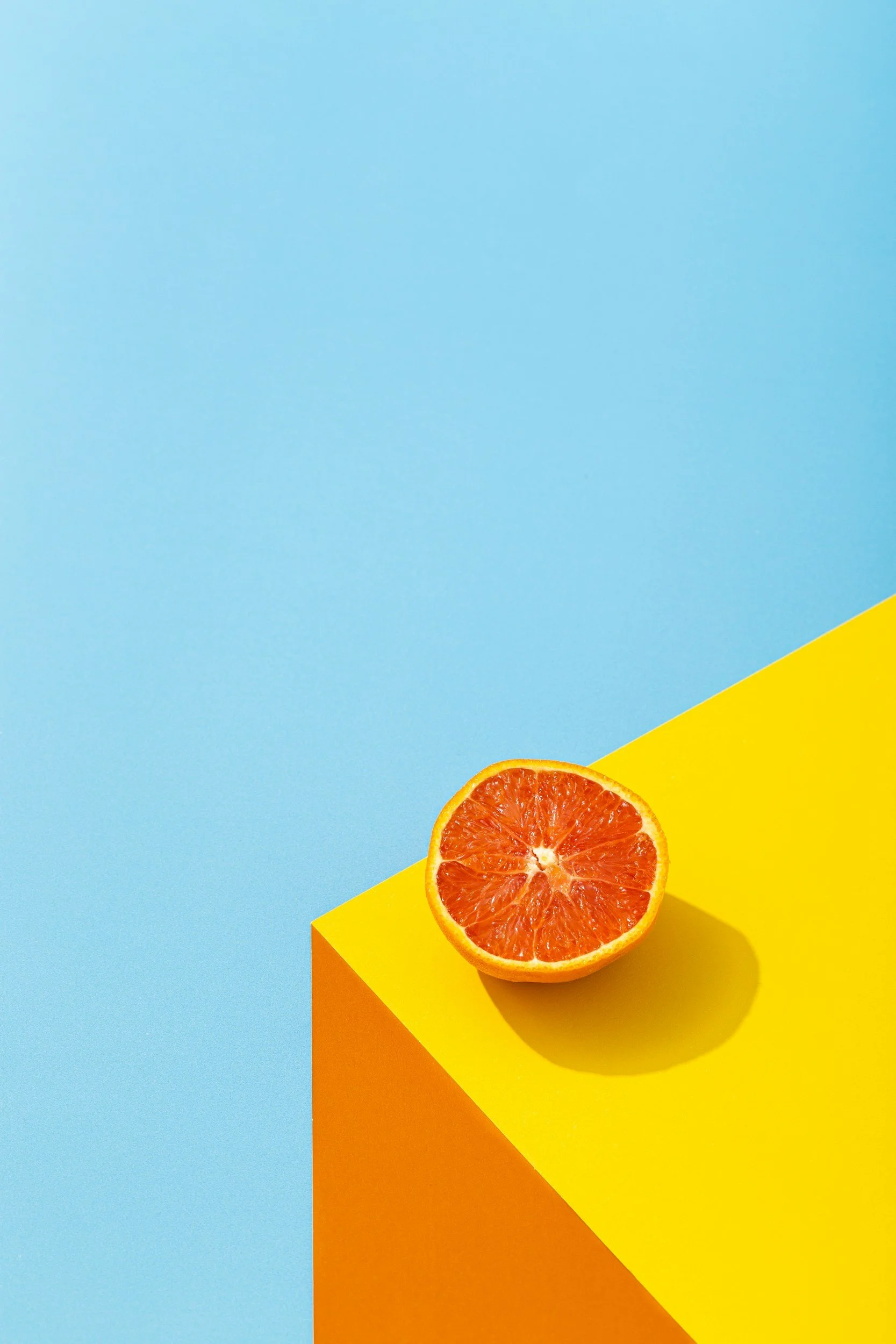 Half a sliced orange on a yellow platform against a blue background.