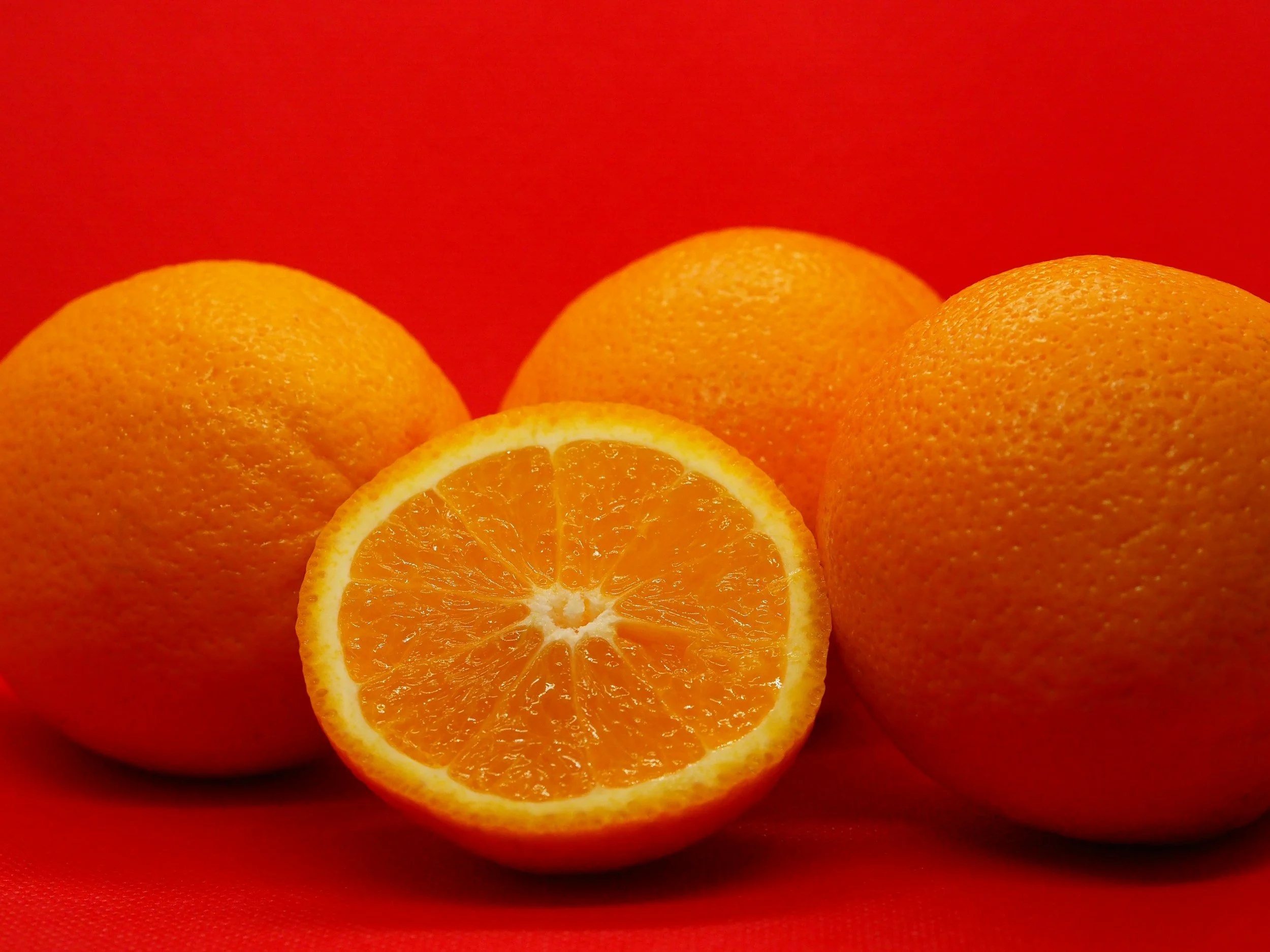 Four whole oranges and one orange cut in half, set against a red background.