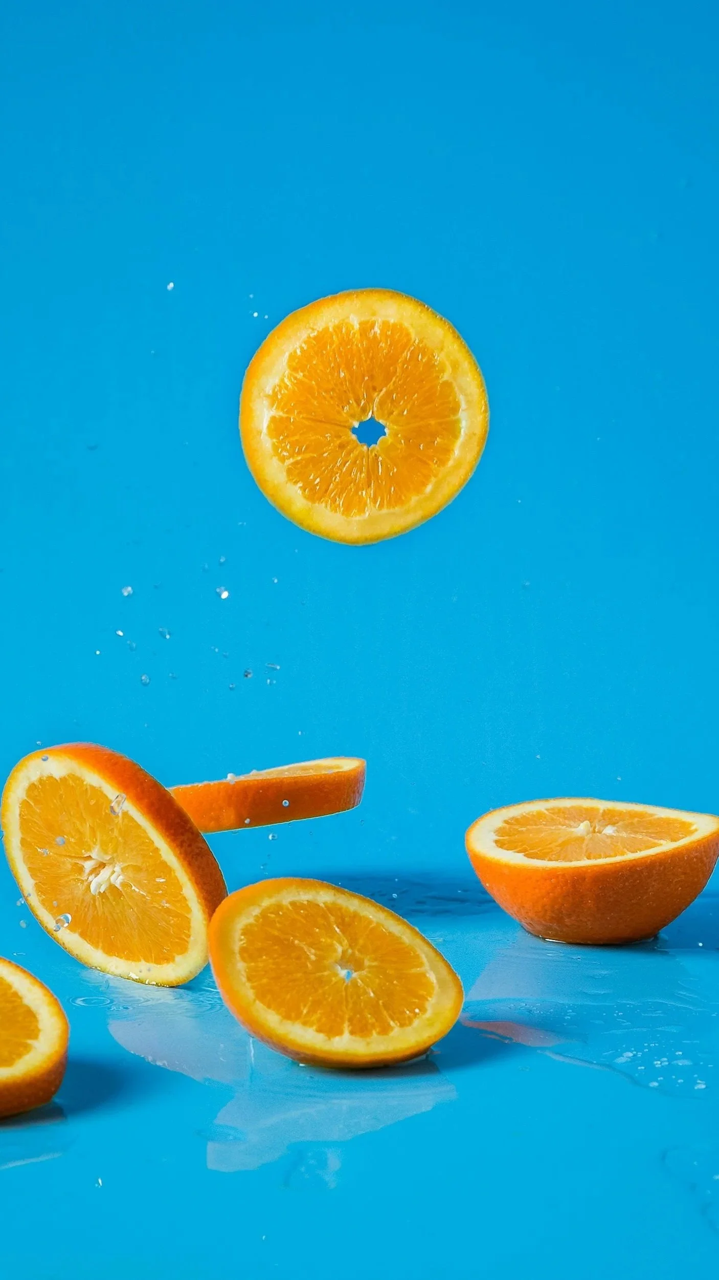 Slices of orange floating against a blue background with water droplets.