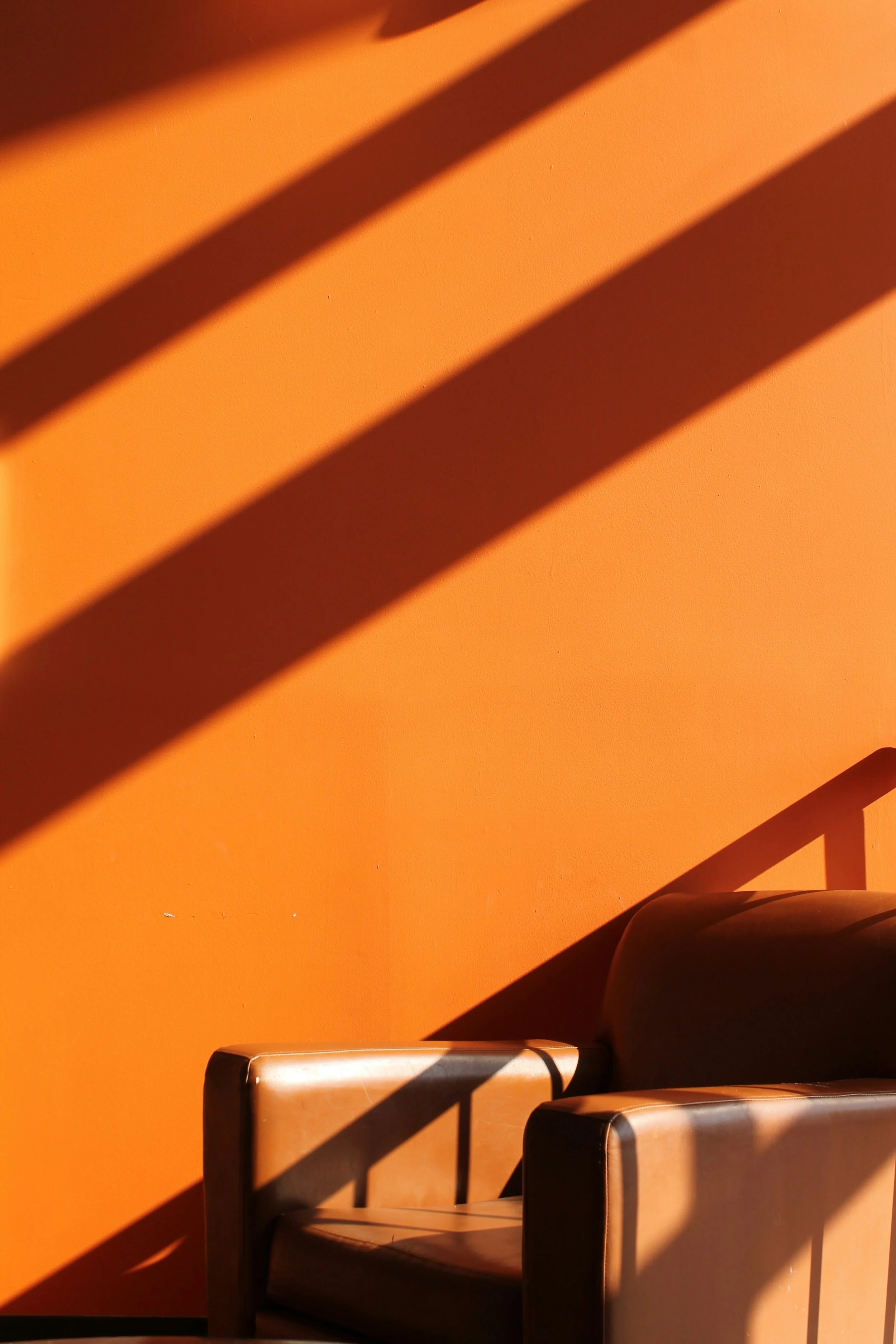 A wooden armchair with shadow lines cast on an orange wall.