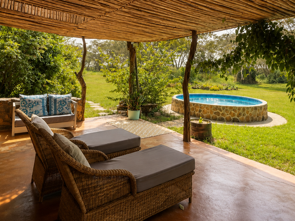 Outdoor patio with wicker lounge chairs, a small sofa with patterned cushions, potted plants, a stone hot tub, and a grassy yard with trees and shrubs.