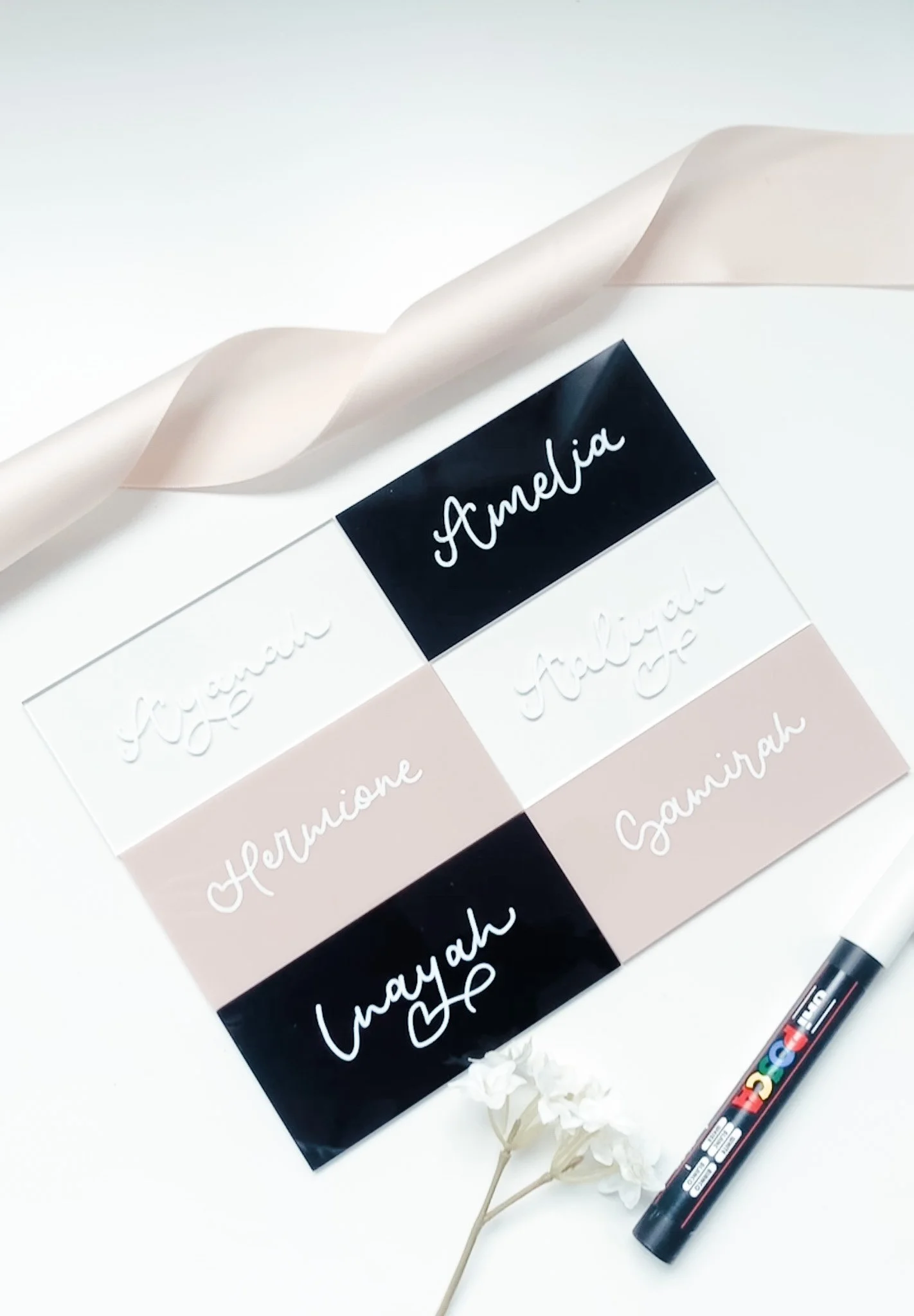 Color chart featuring names of various shades of taupe, black, white, and beige, with a black marker and white flowers nearby.