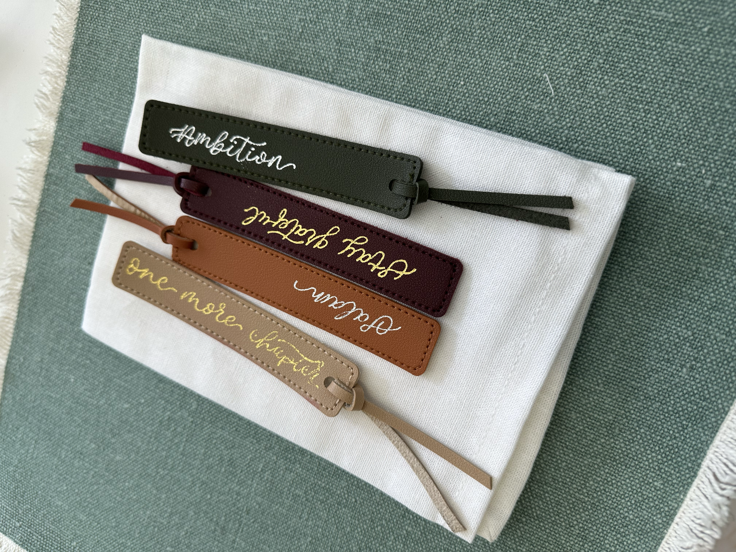Four leather color swatches with embroidered inspirational phrases, placed on a folded white napkin on a green table.