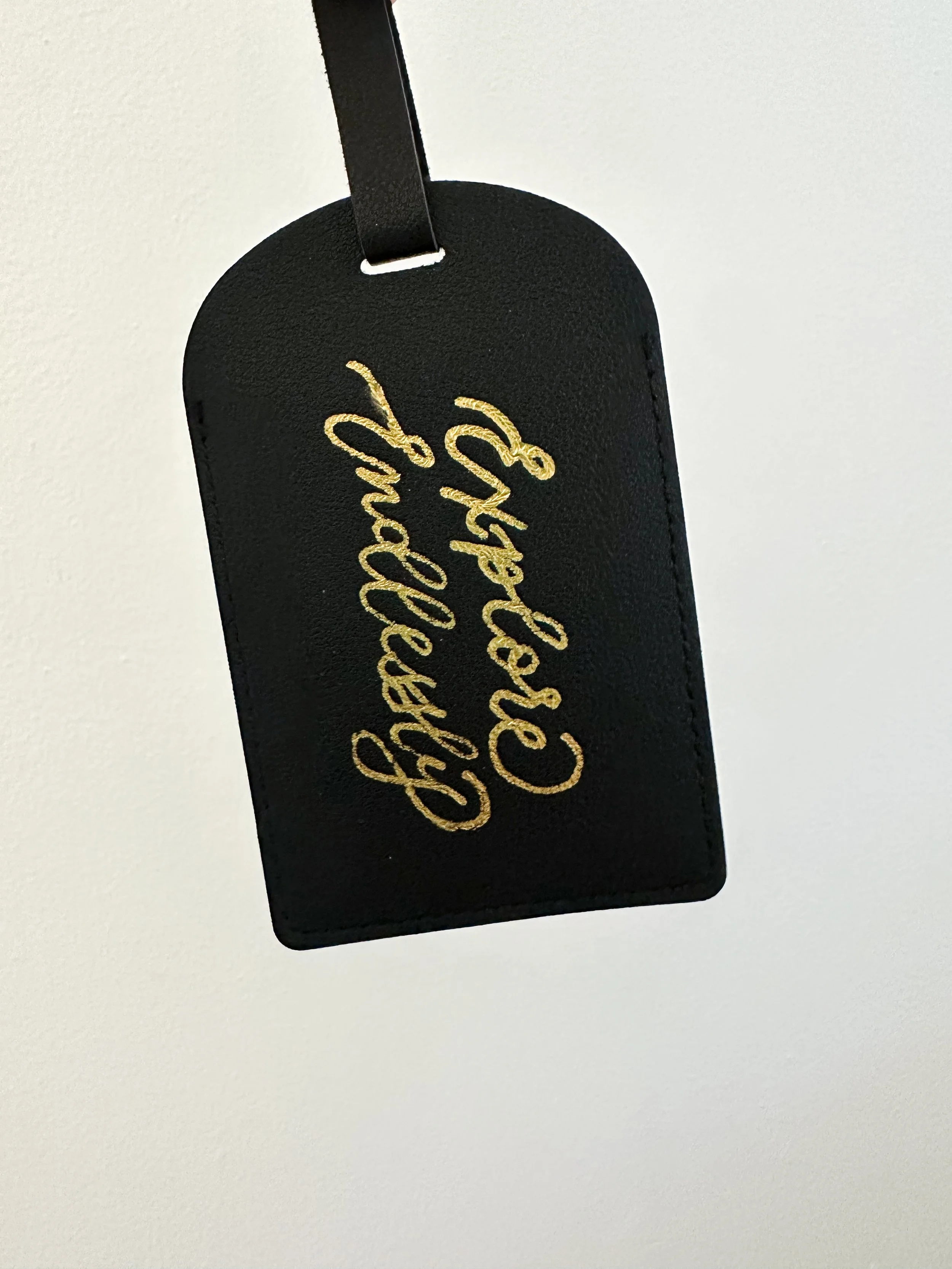 Black leather luggage tag with gold embroidered cursive text.