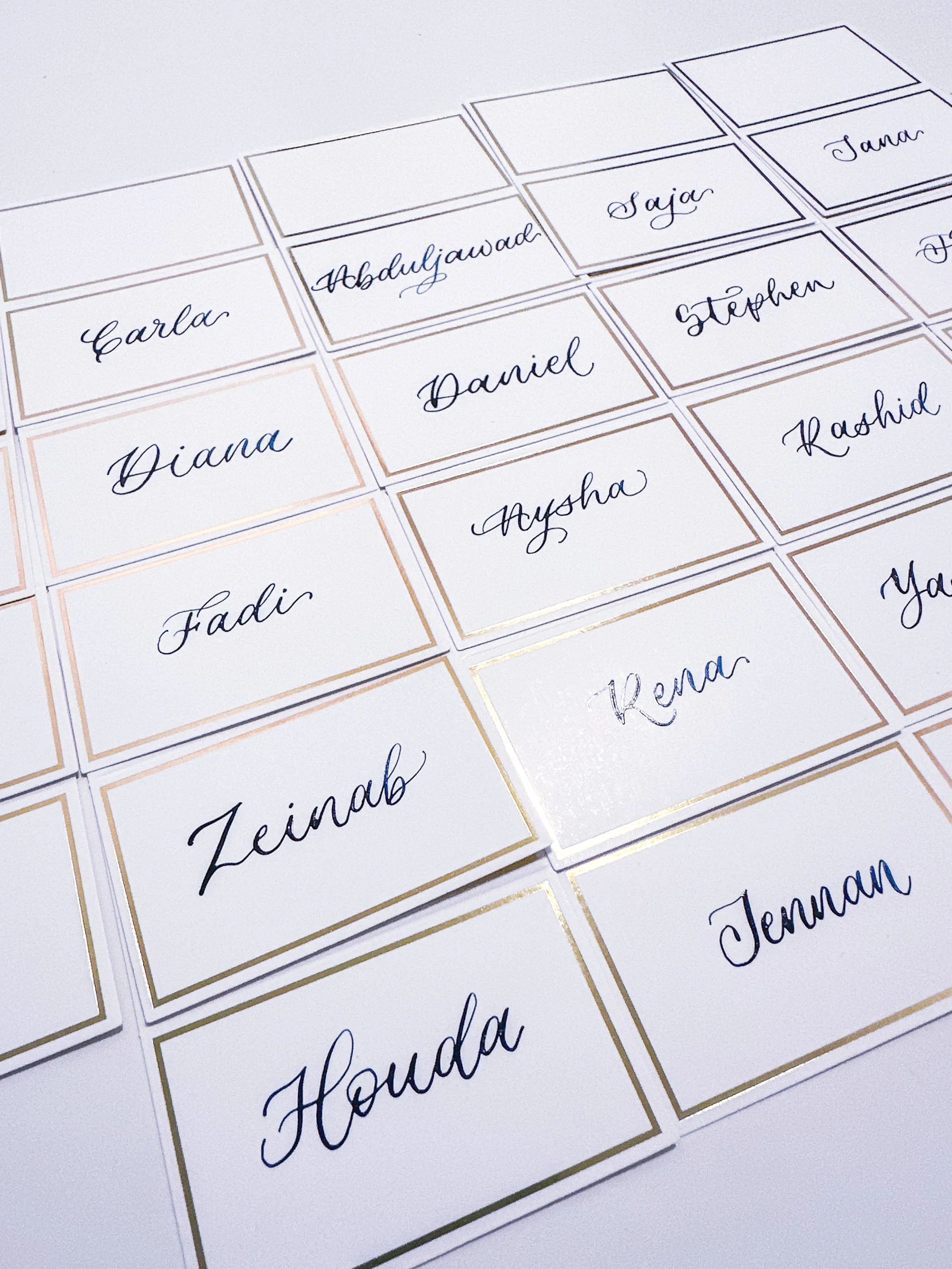 Close-up view of white name tags with cursive names written in blue ink, arranged in an overlapping pattern on a white surface.