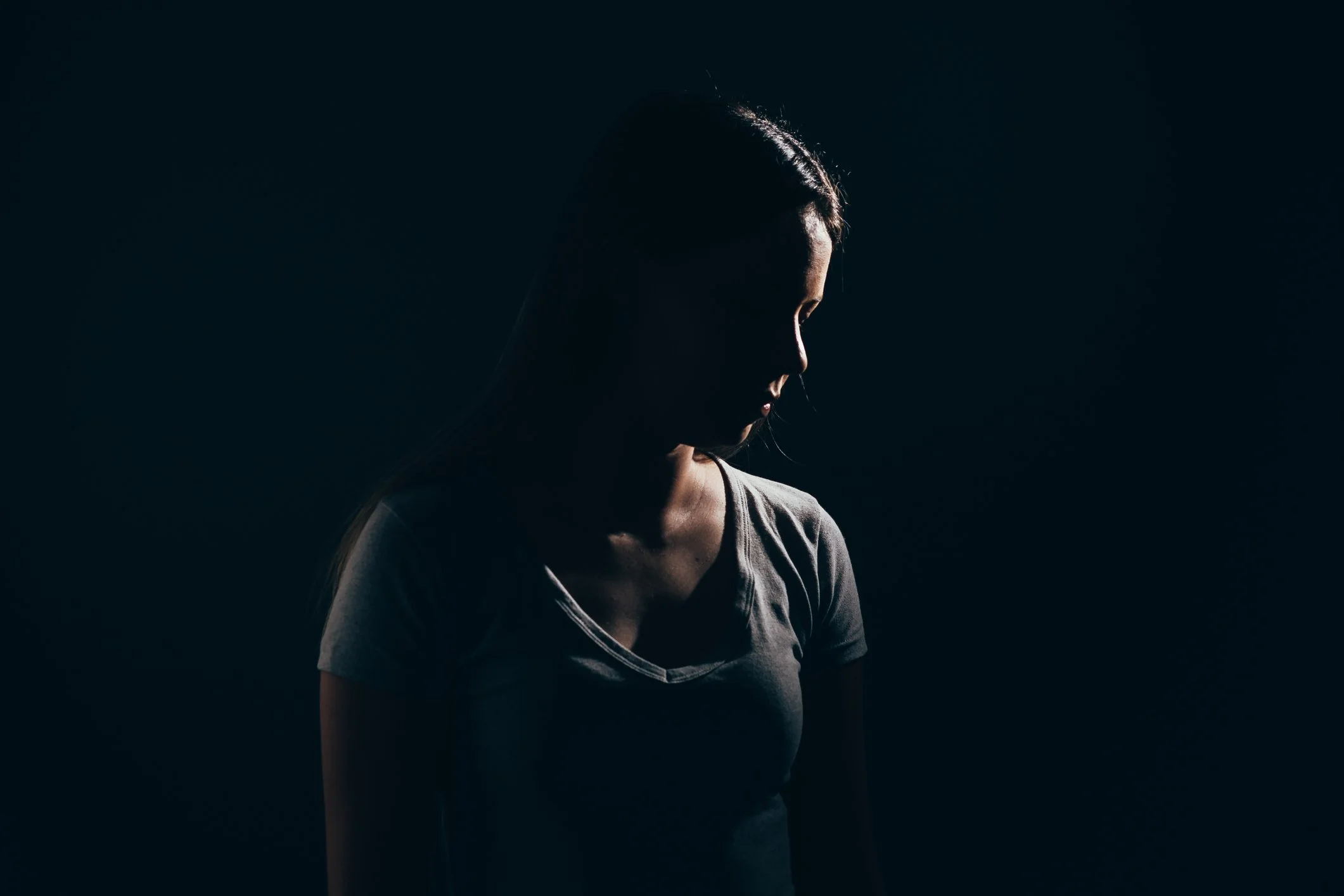 A person standing in low-key, dramatic side-lighting against a dark background, creating a silhouetted profile effect.