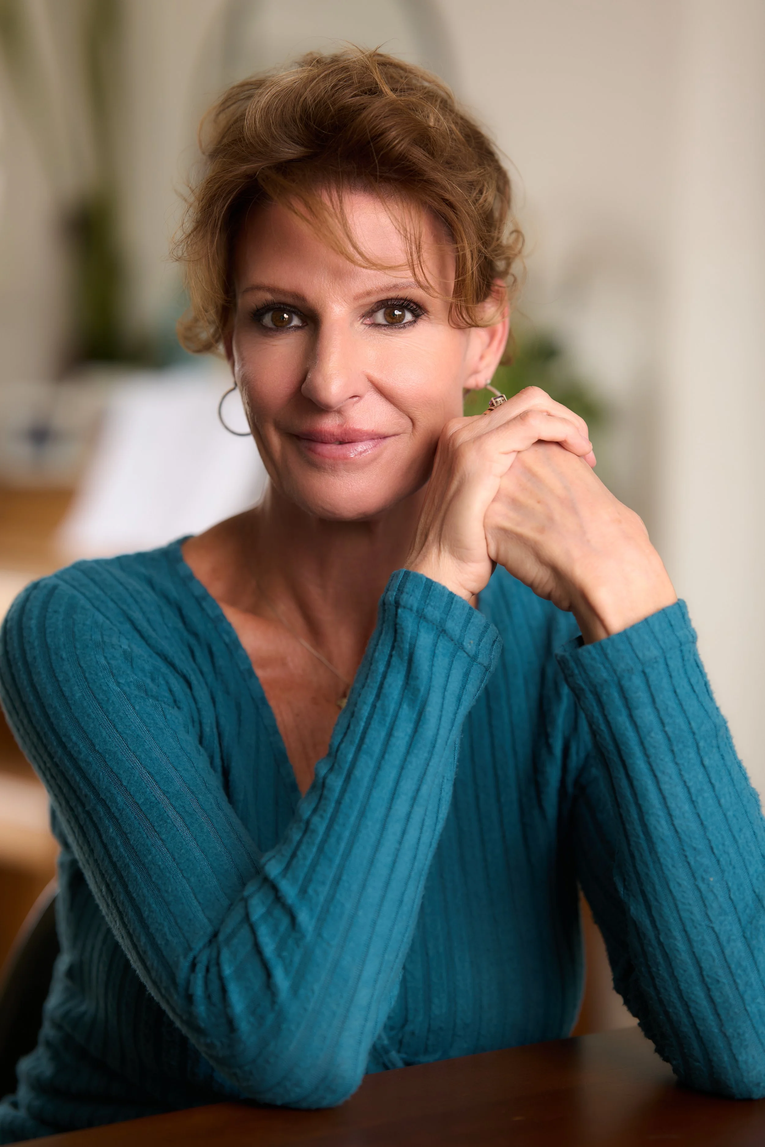 A woman with short, curly brown hair and wearing earrings and a red top.