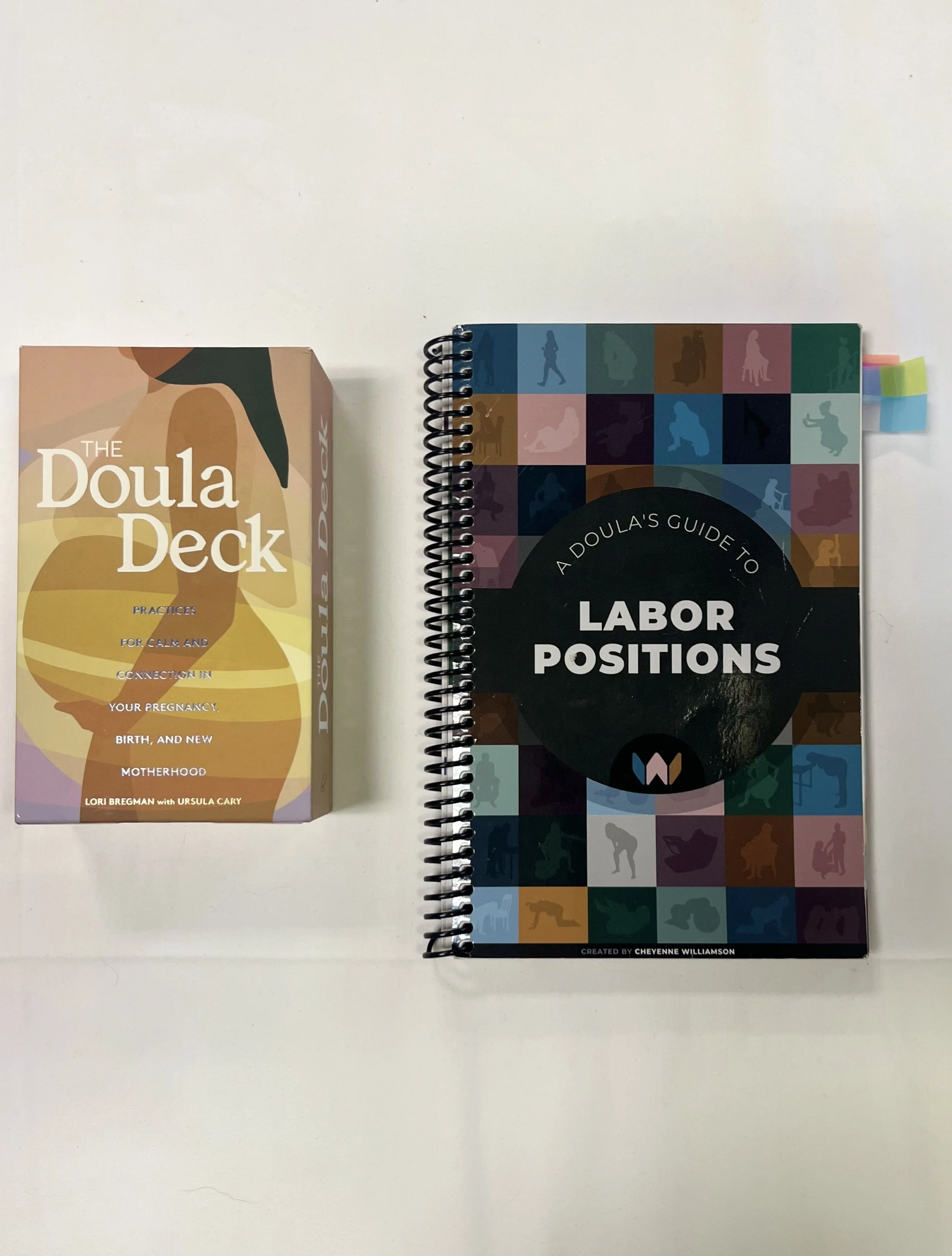 A box titled 'The Doula Deck' and a spiral notebook titled 'A Doula's Guide to Labor Positions' on a white surface.